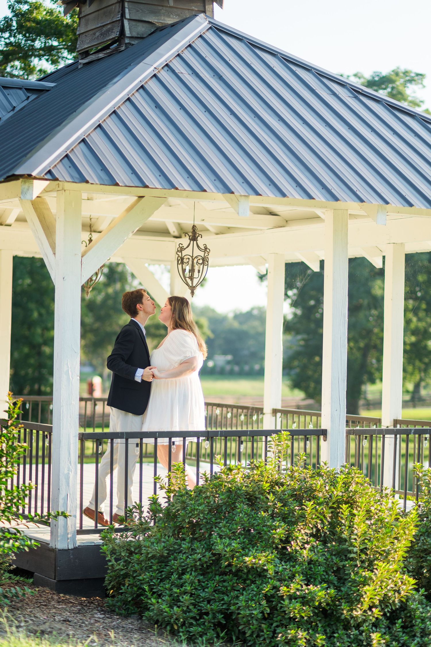 Bride and groom sharing a romantic kiss inside a white gazebo with a chandelier at golden hour.