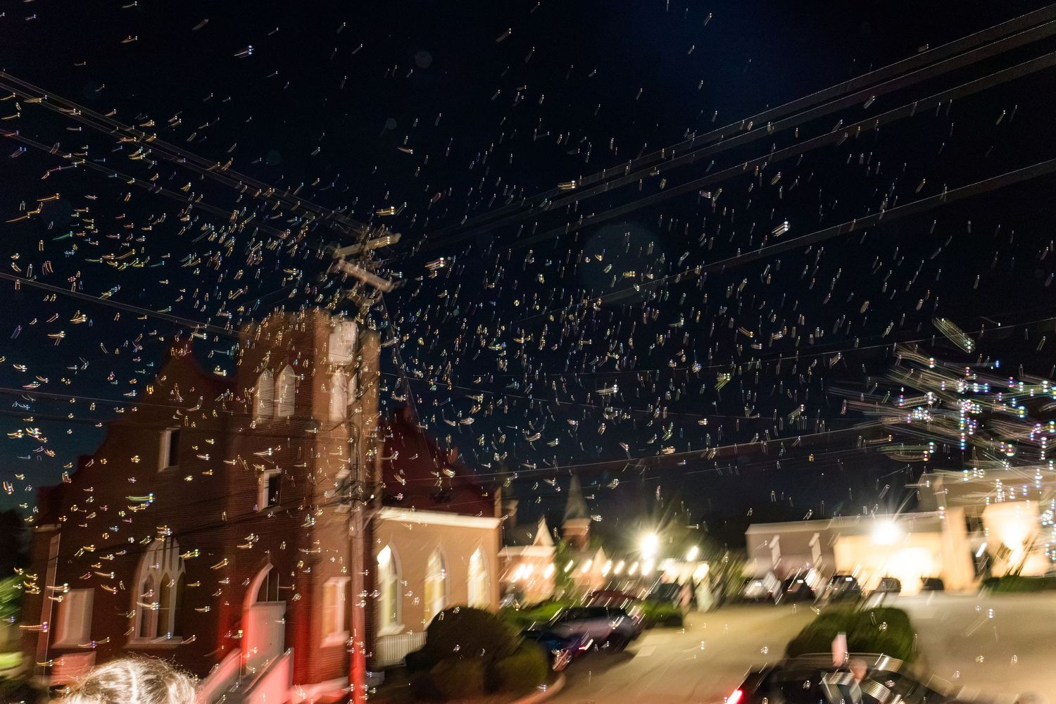 Confetti fills the night sky outside illuminated red brick church during outdoor wedding celebration.