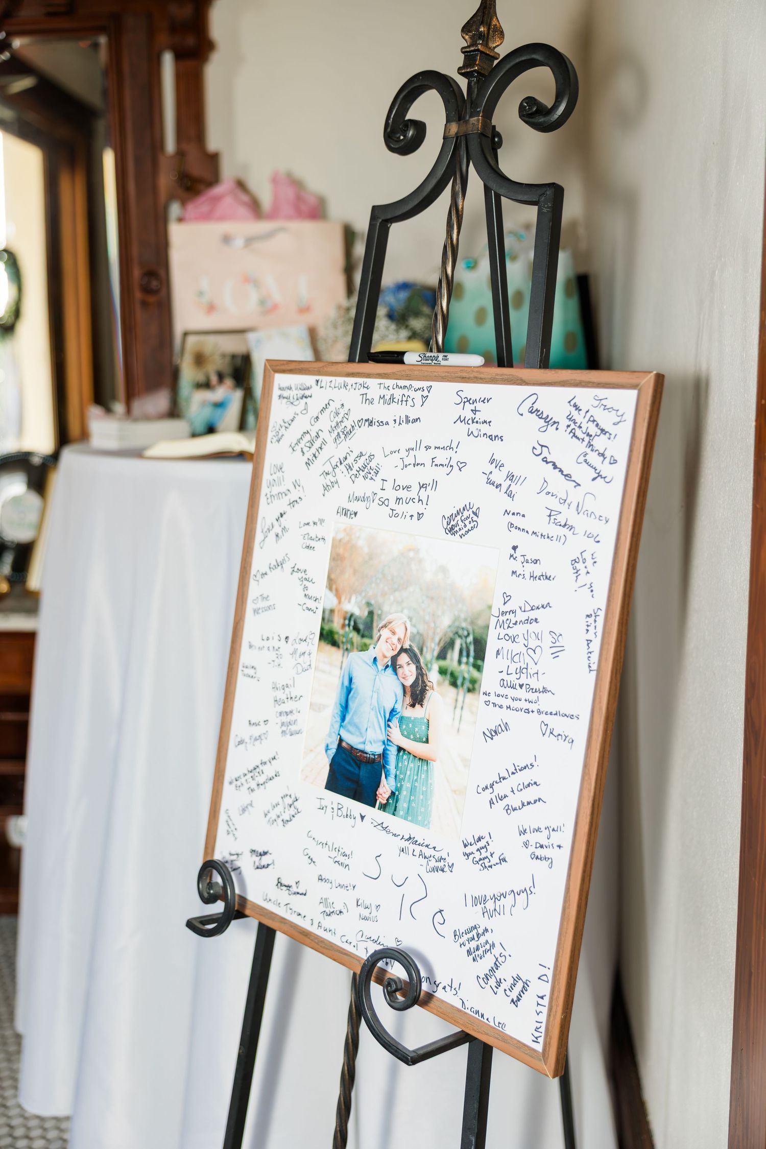 Wedding guest book display board with couple photo surrounded by signatures on decorative easel at reception.