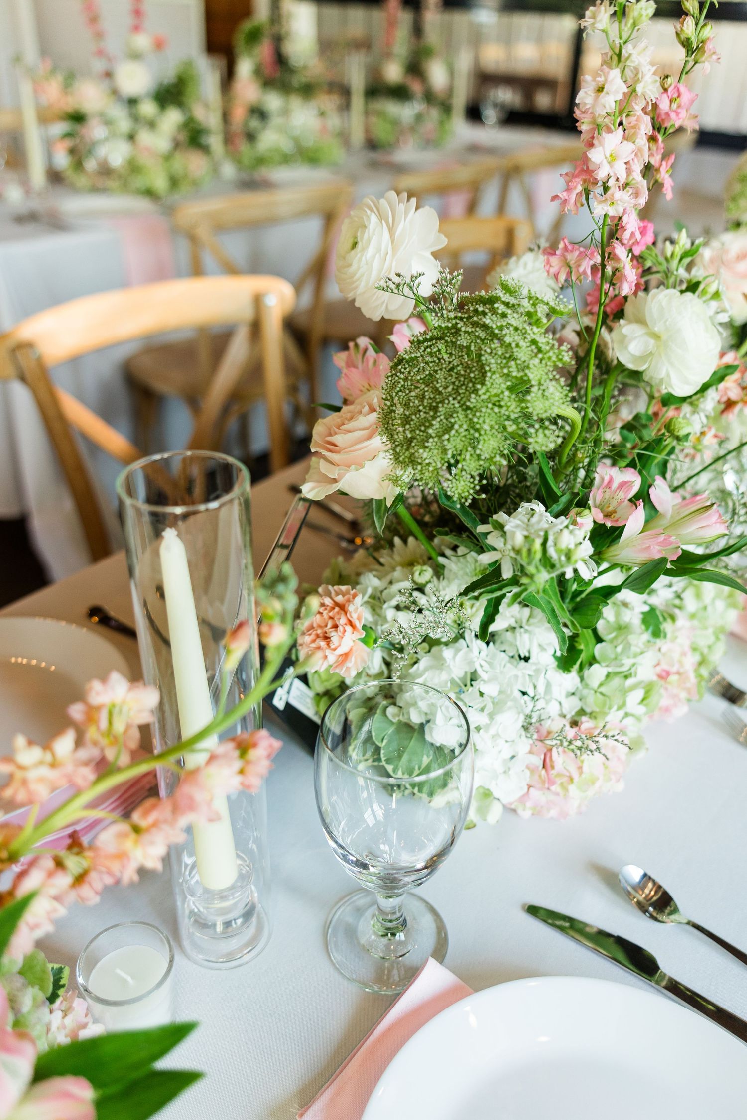 Elegant wedding reception table with pink and white floral centerpiece, candles, and place settings.