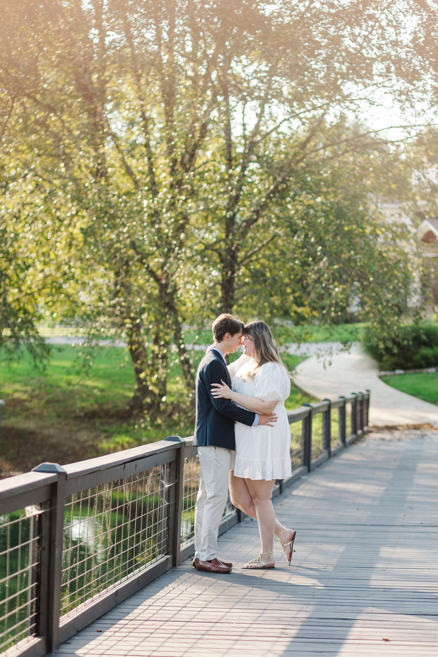 Couple sharing a romantic kiss on a wooden bridge surrounded by golden autumn trees in soft sunlight.