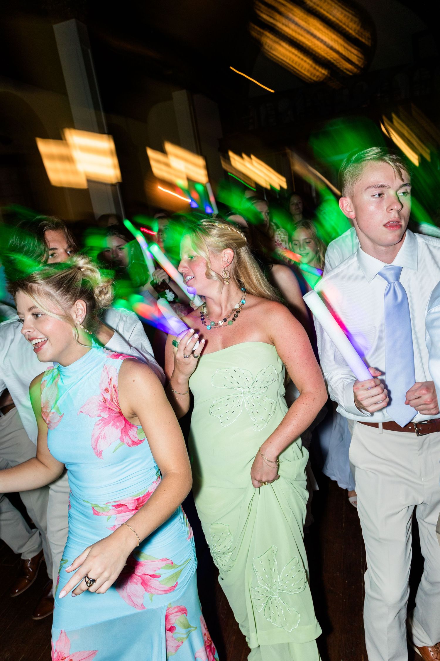 Guests dancing with glow sticks under colorful lights at an energetic wedding reception.