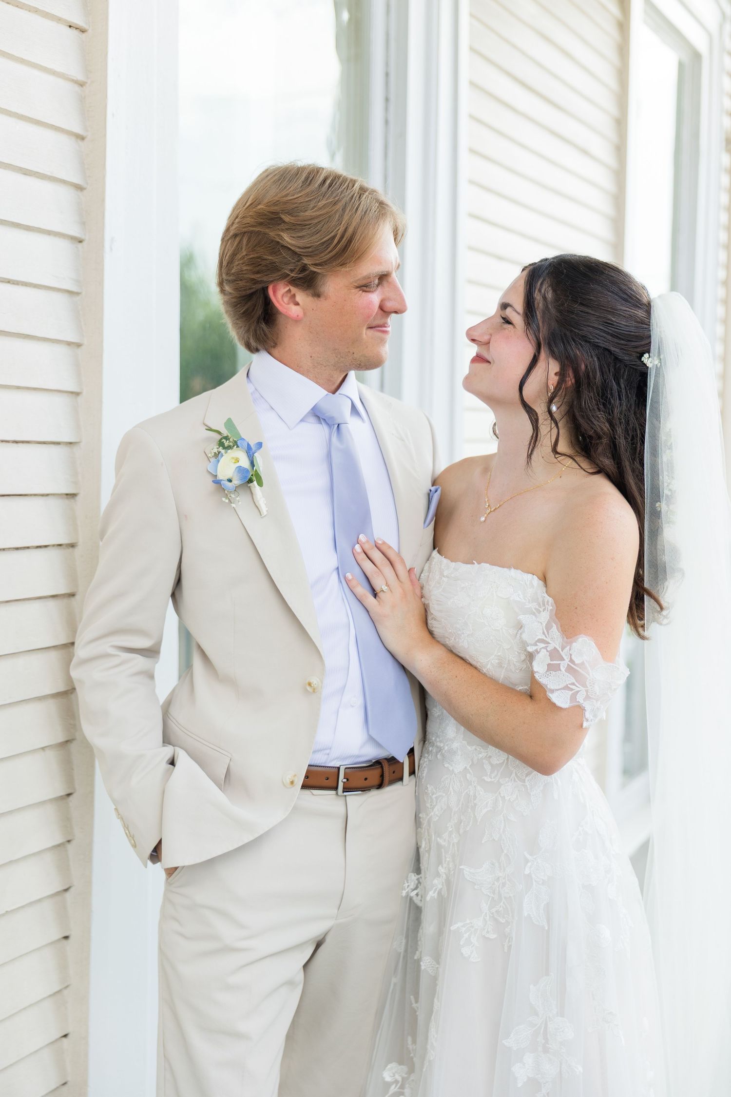 Bride and groom share a romantic moment outside, groom in tan suit with blue tie and bride in lace gown.