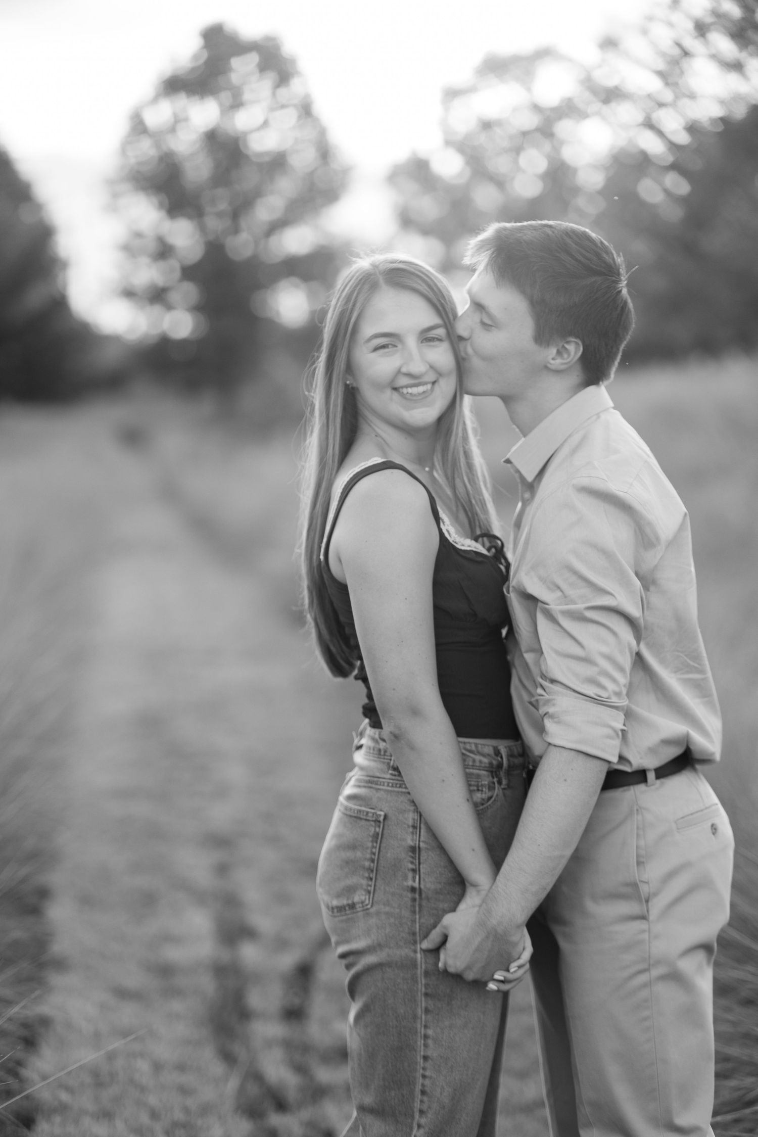 A black and white photo of a couple holding hands as the man kisses her cheek.