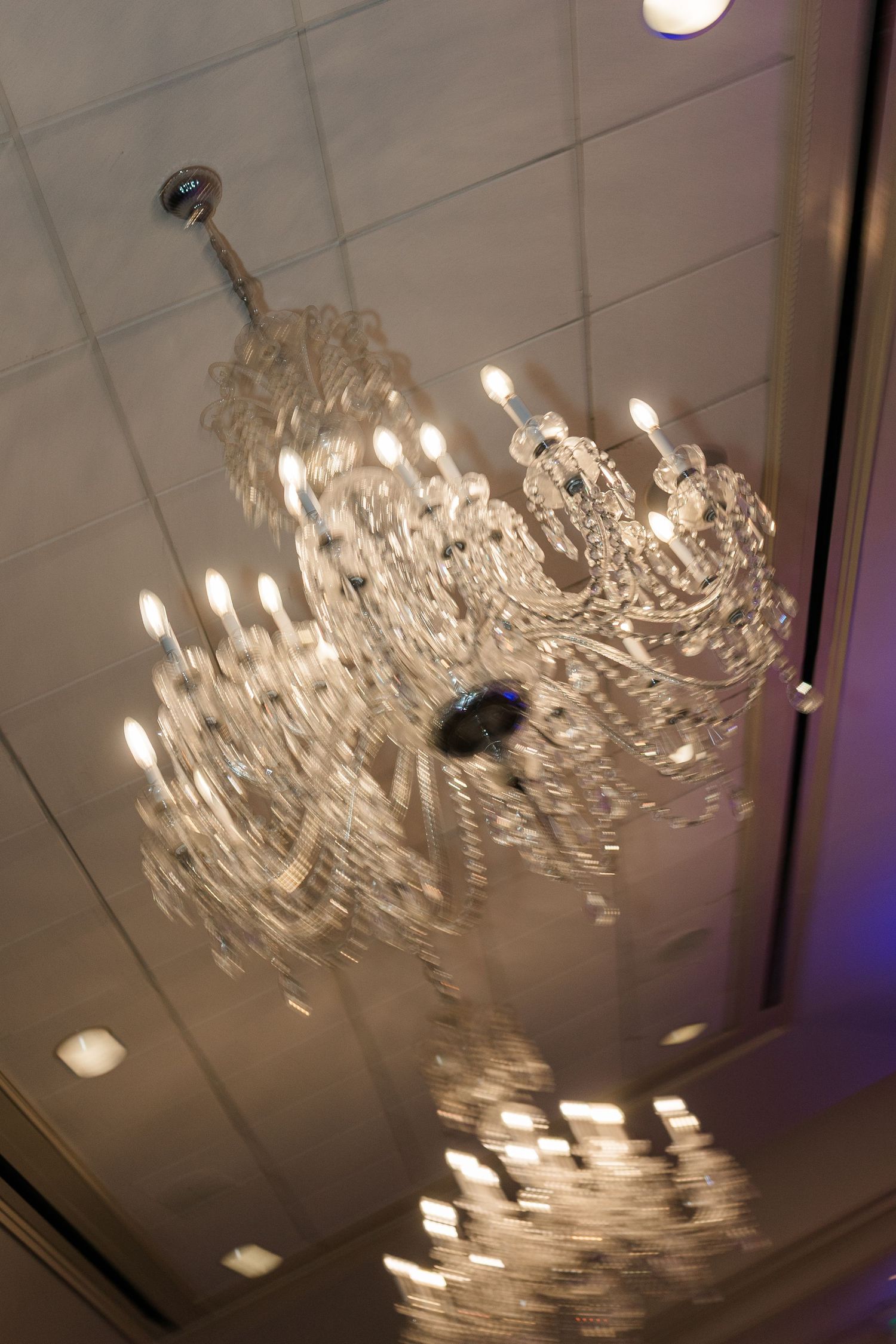 Ornate crystal chandelier with glowing candle lights reflecting off tiled ceiling.