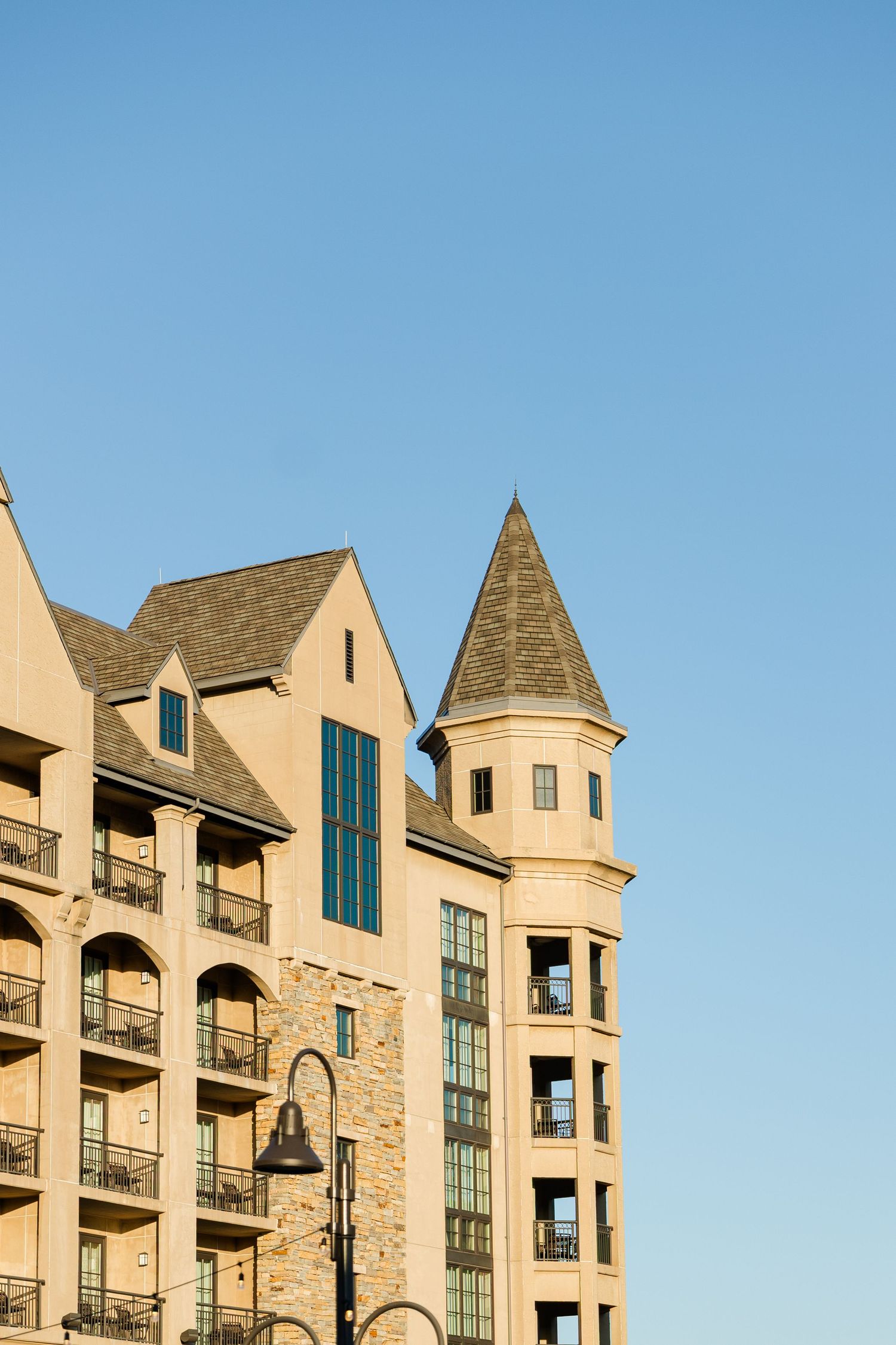 Elegant multi-story hotel building with castle-like turret, stone facade, and balconies against a clear blue sky.