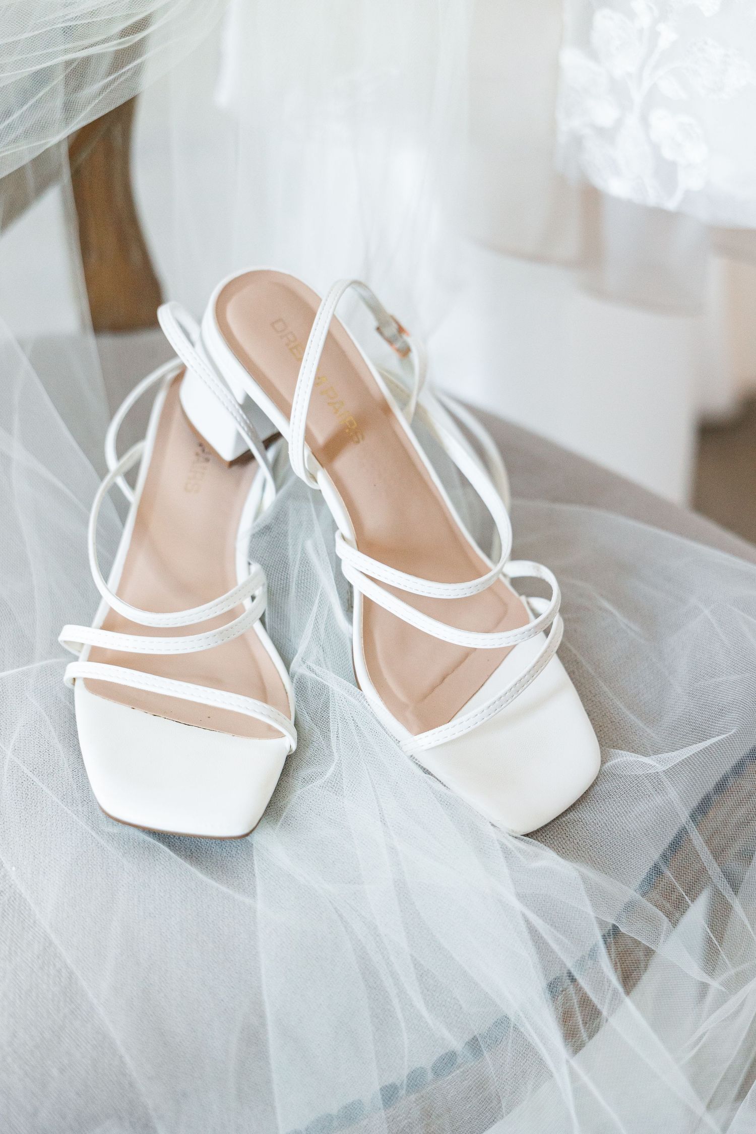 White strappy block heel wedding sandals resting on a sheer bridal veil.