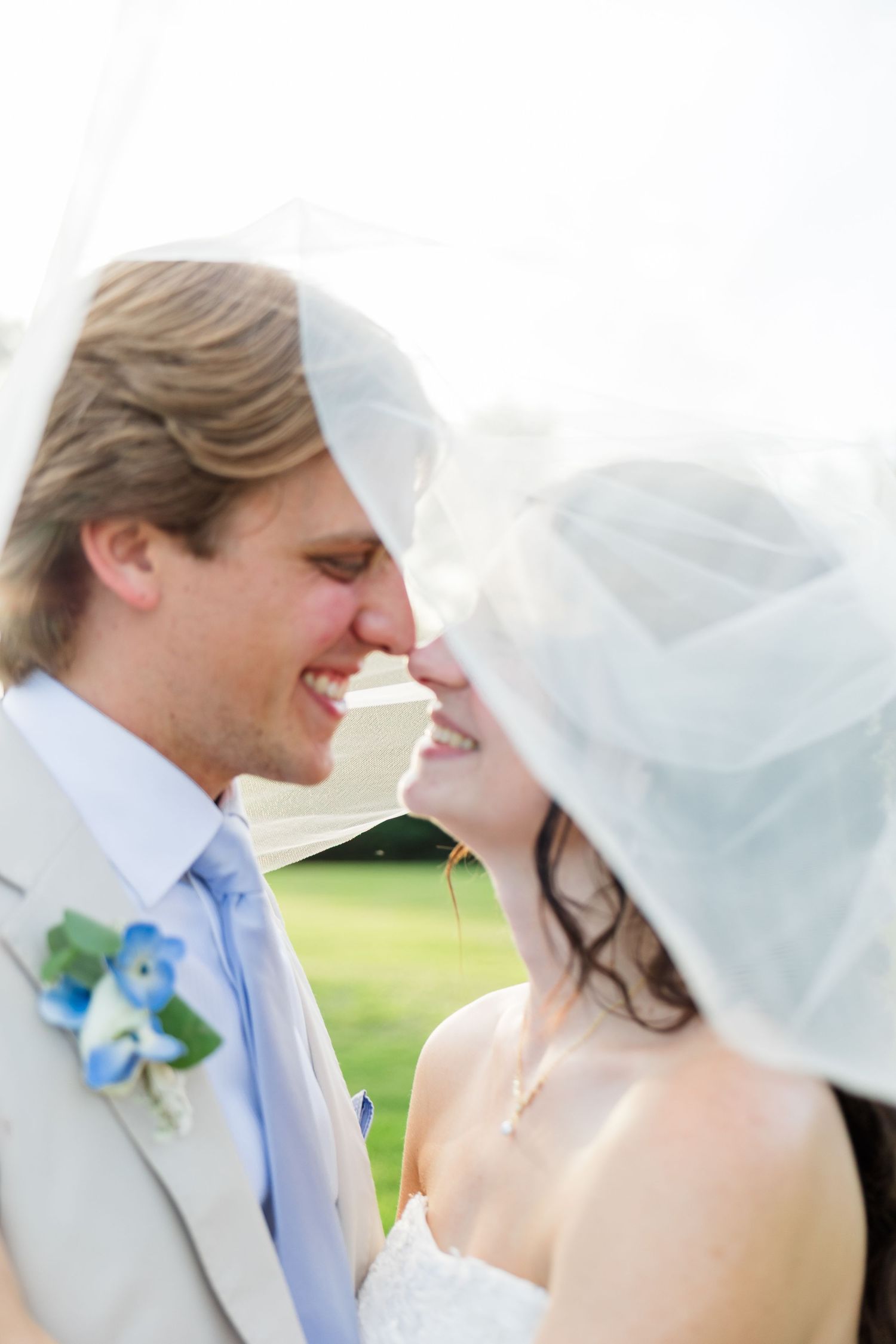 Happy bride and groom sharing a romantic moment under a flowing veil, smiling face to face on their wedding day.