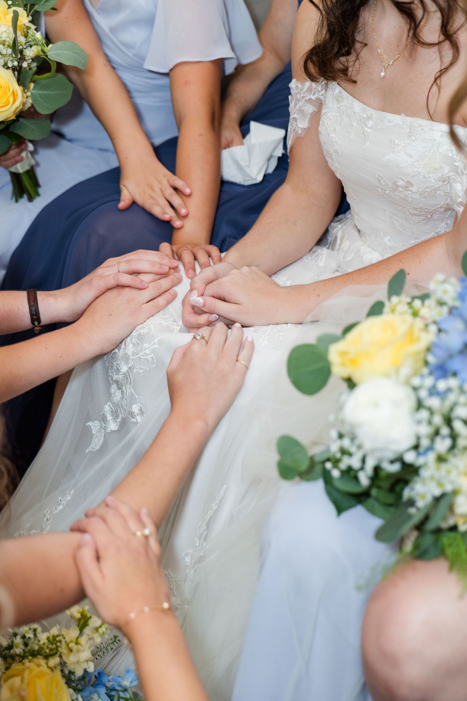 Bride and bridesmaids joining hands together in a circle during wedding preparations.