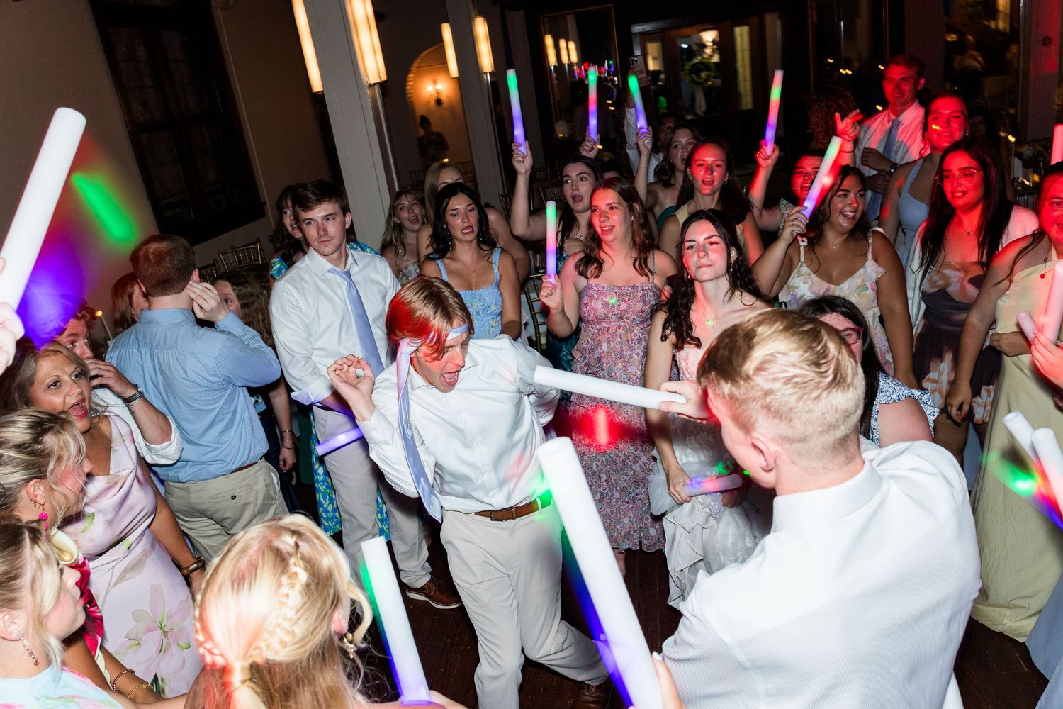 Energetic wedding reception dance floor with guests holding colorful LED glow sticks.