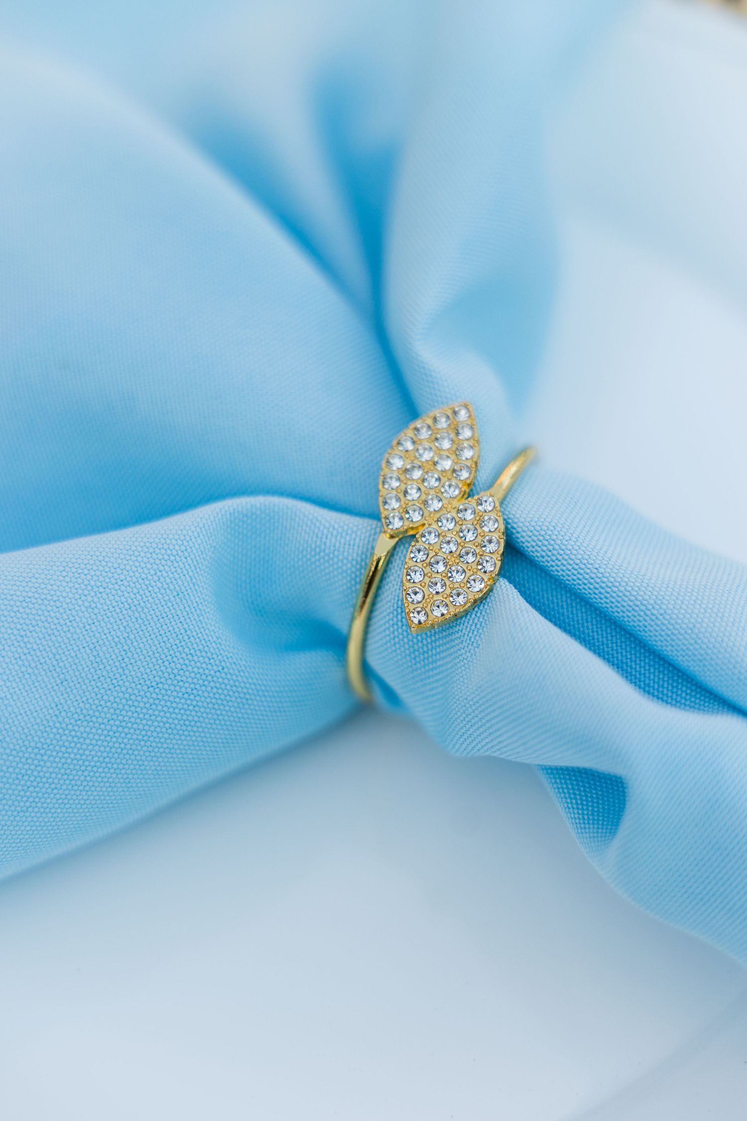 Gold leaf ring with diamond pavé setting displayed on soft blue fabric.