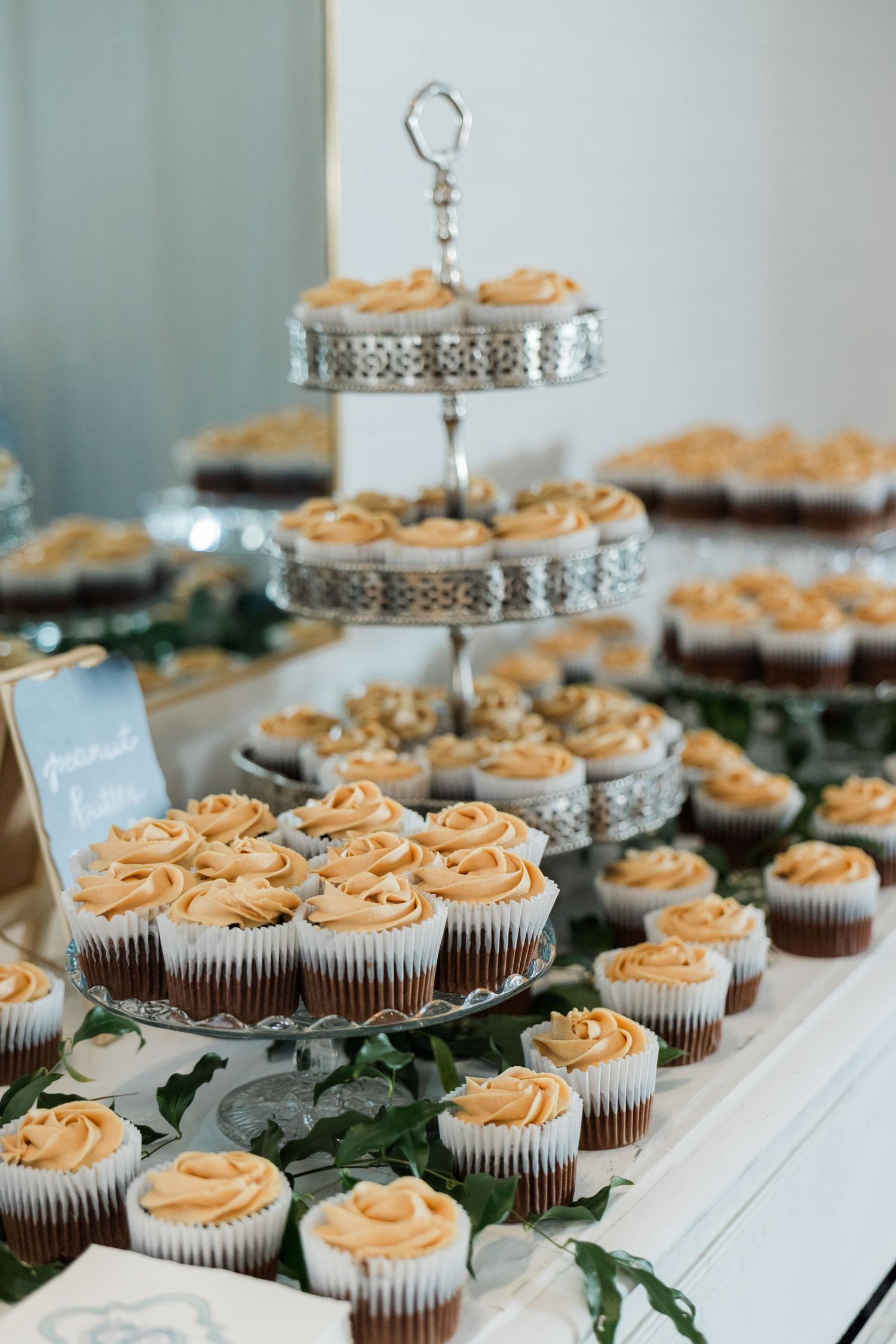 Elegant wedding dessert table with tiered silver stands displaying chocolate cupcakes topped with swirled caramel frosting.