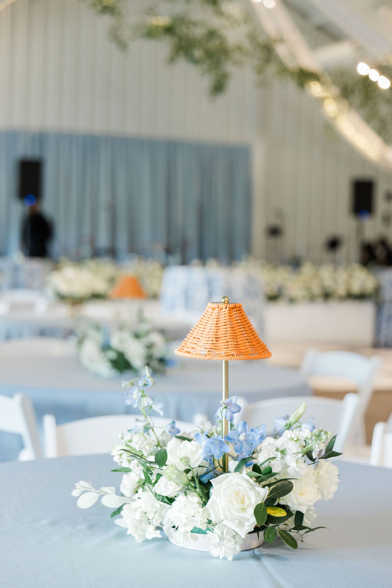 Elegant wedding reception table with white and blue floral centerpiece and wicker lamp.