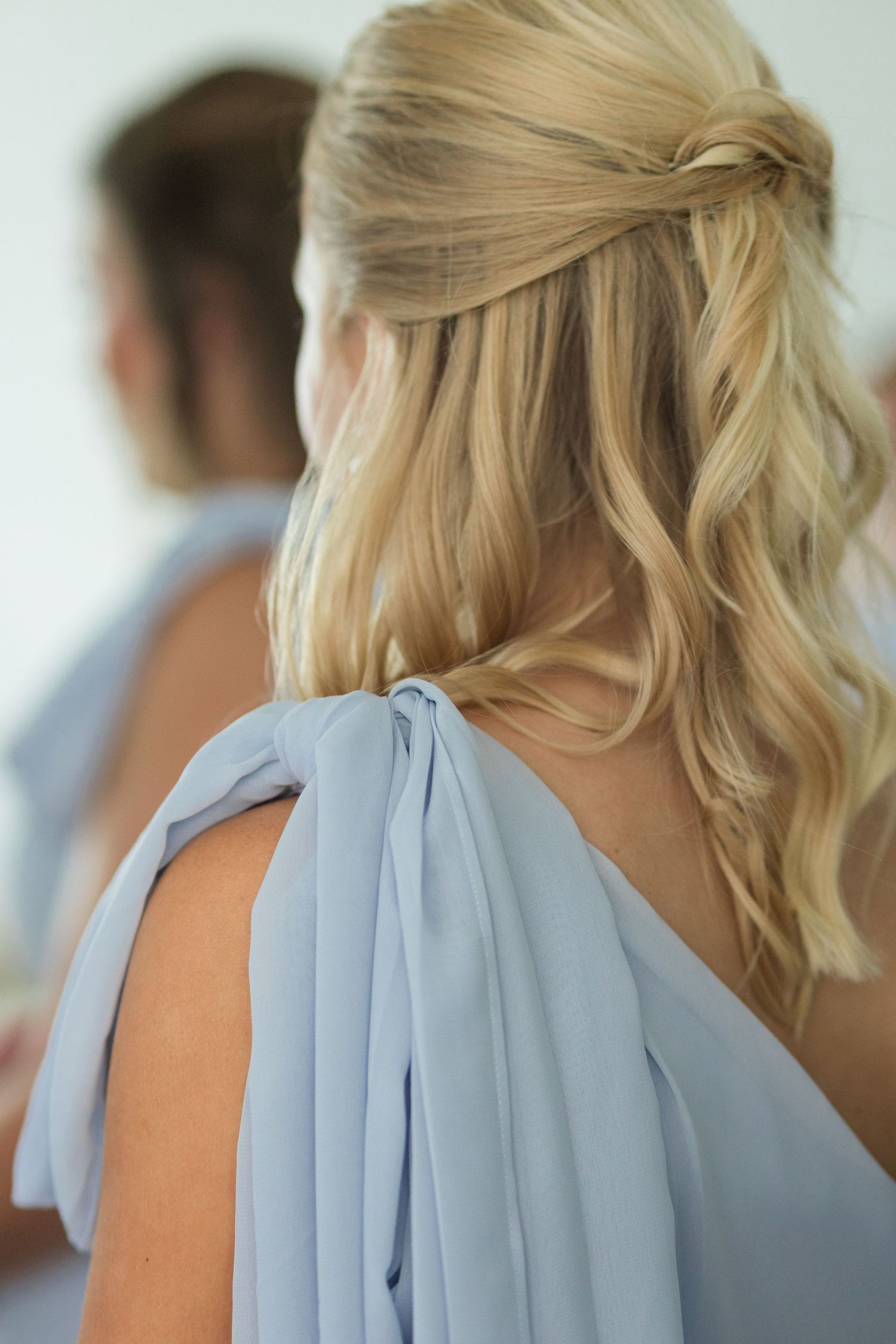 Close-up of blonde bridesmaid in dusty blue chiffon gown with elegant half-up wavy hairstyle.