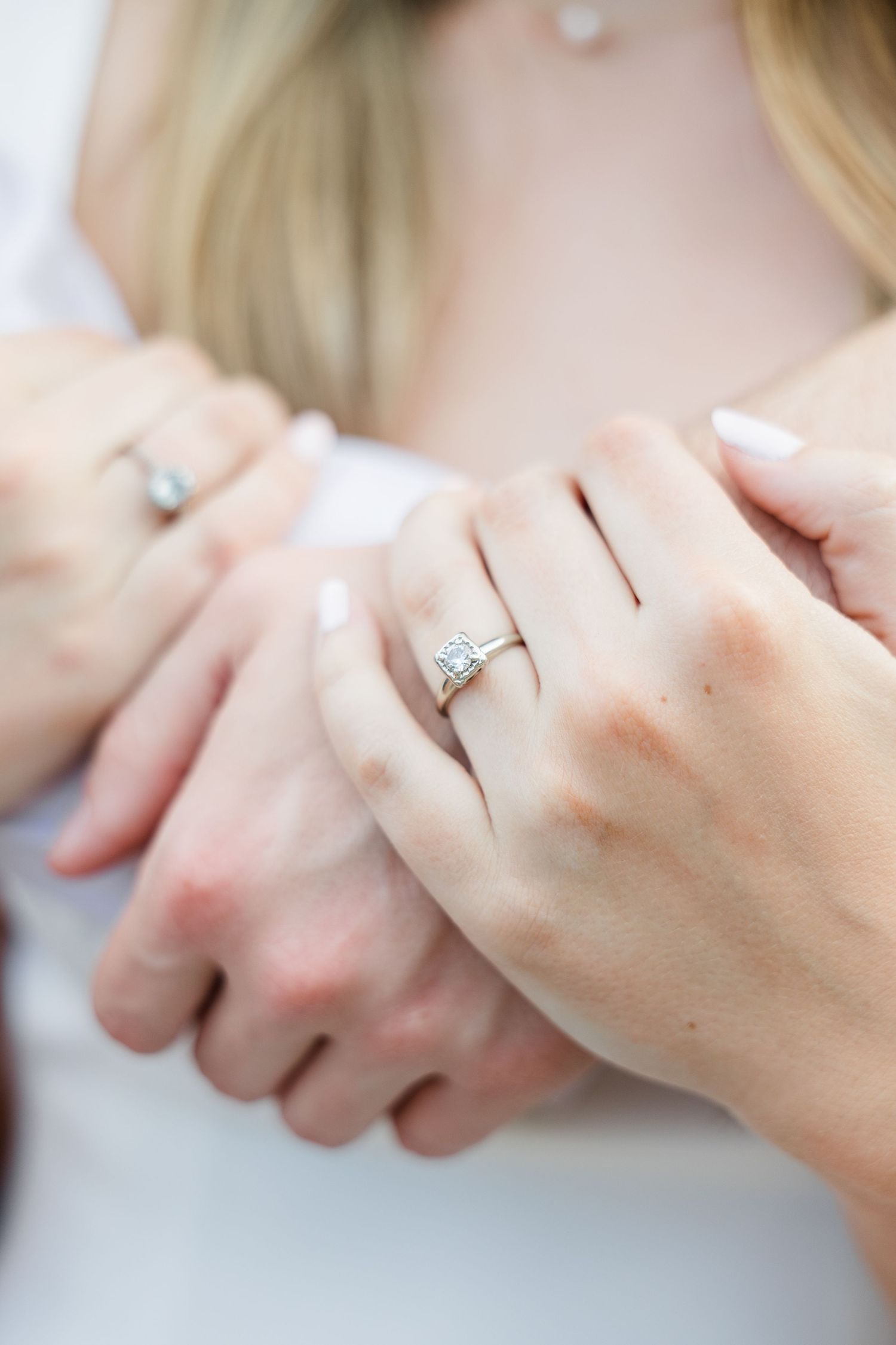 Close-up of an engagement ring with a halo diamond setting on a woman's hand held by her partner.