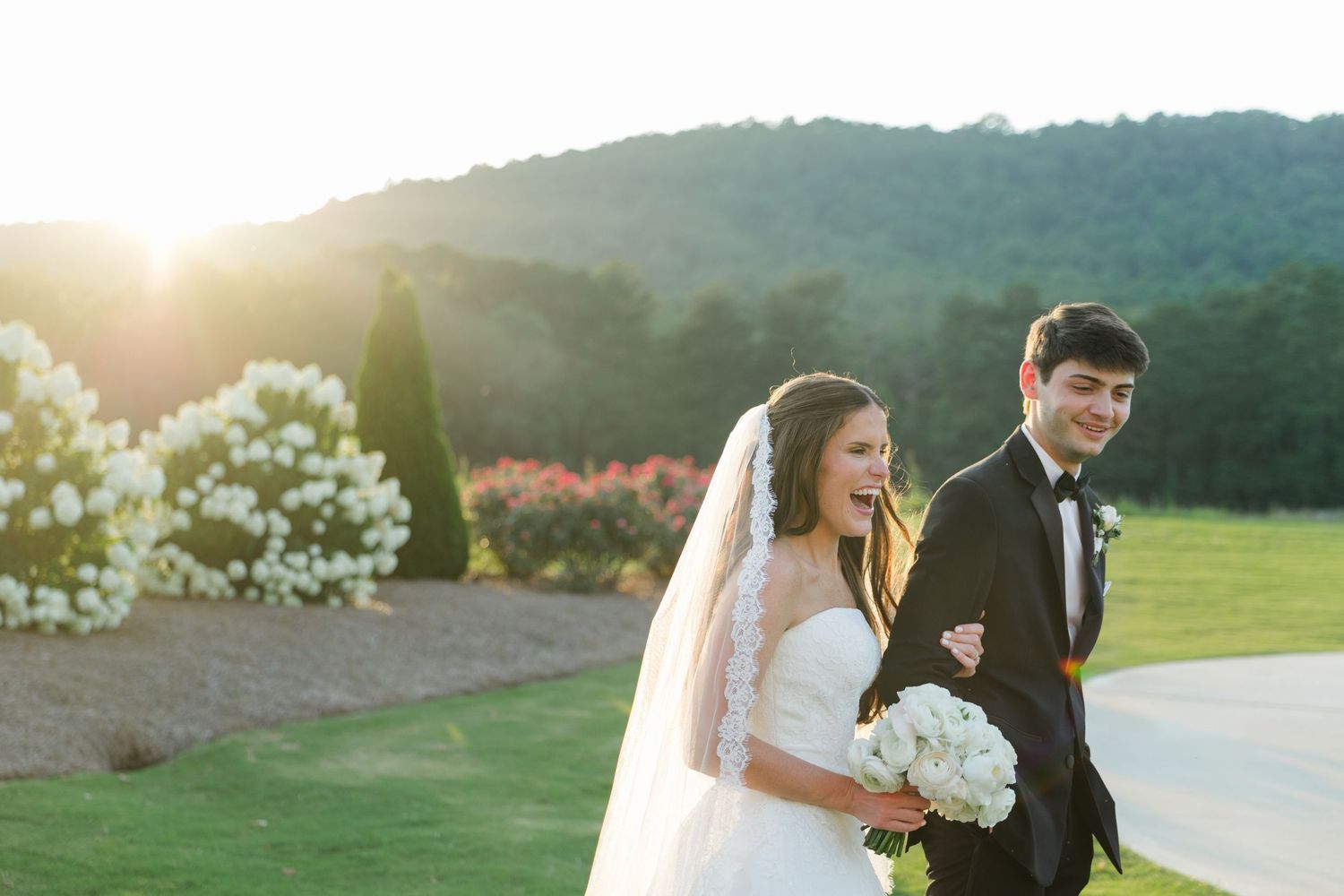 Bride and groom walk together at sunset with mountain views and white hydrangeas at an outdoor wedding venue.