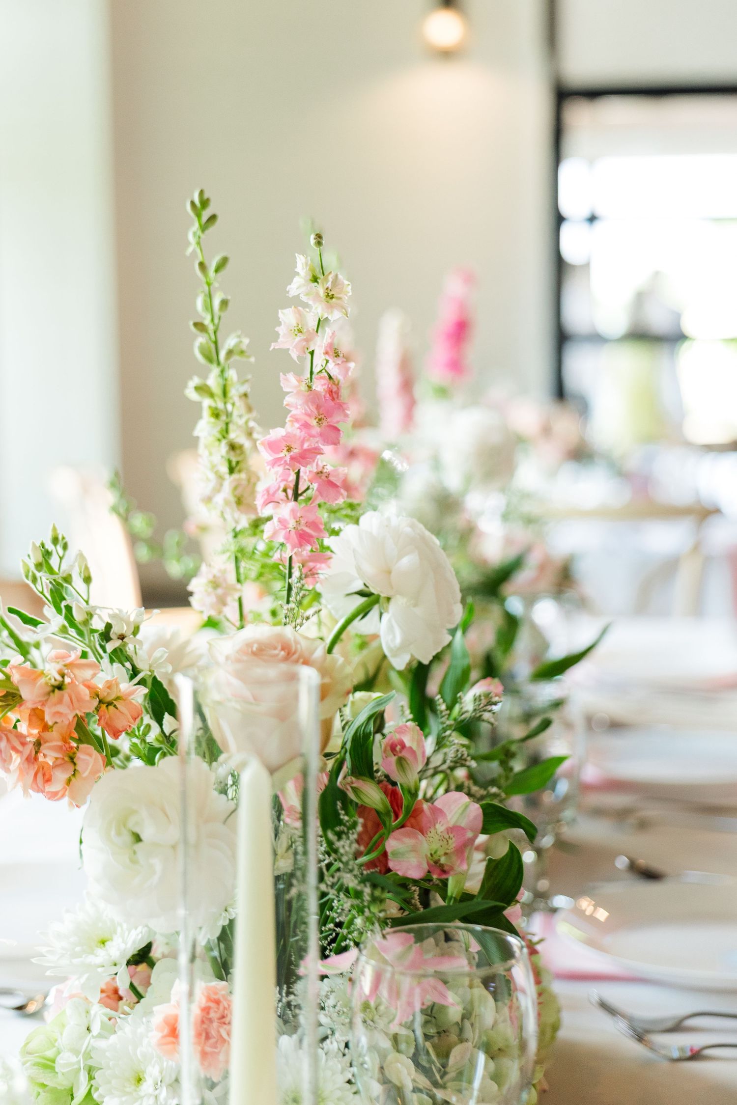 Elegant wedding table centerpiece with pink snapdragons, white ranunculus, and peach blooms in glass vases with taper candles.