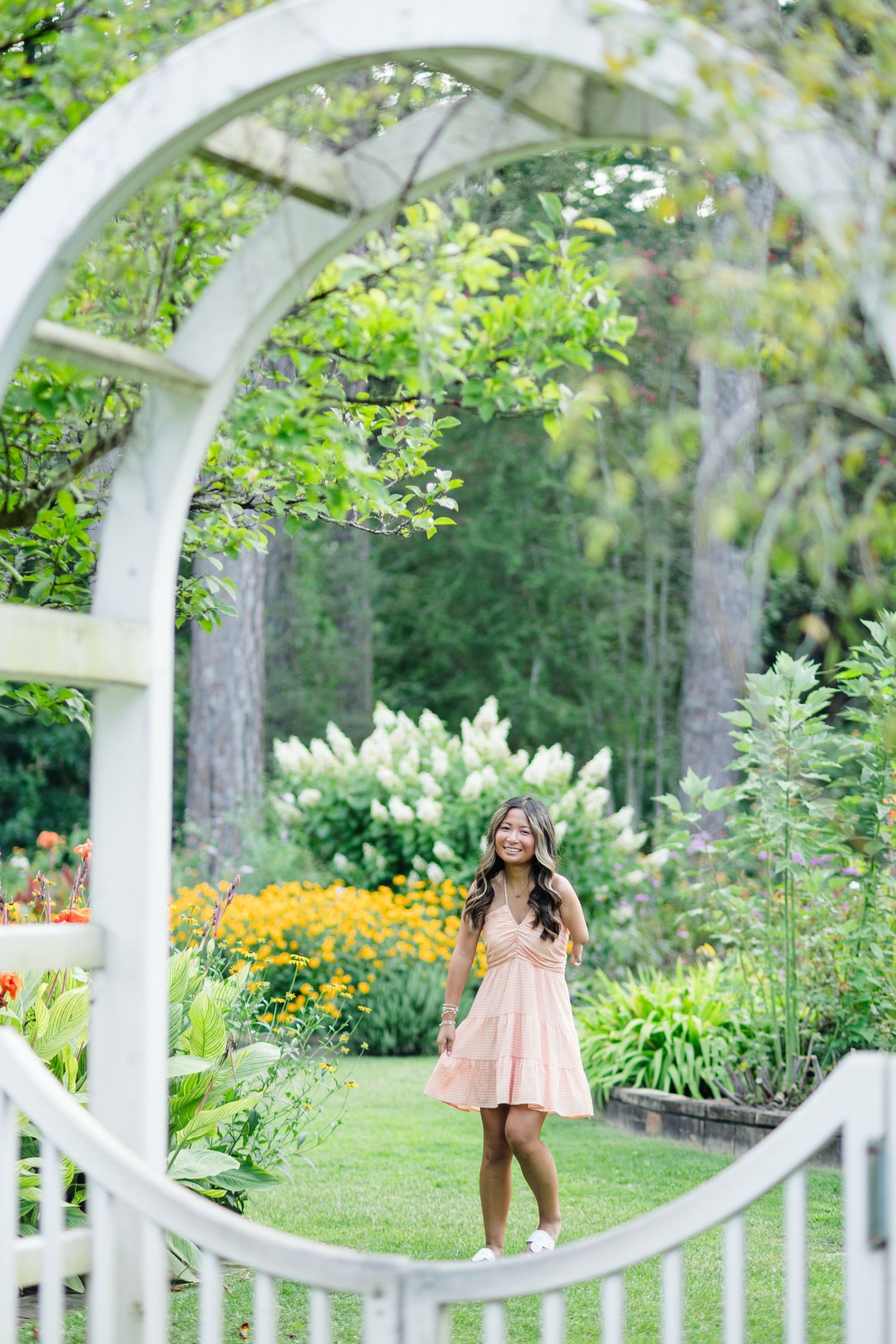 Young woman in peach dress standing in garden framed by white circular arbor.