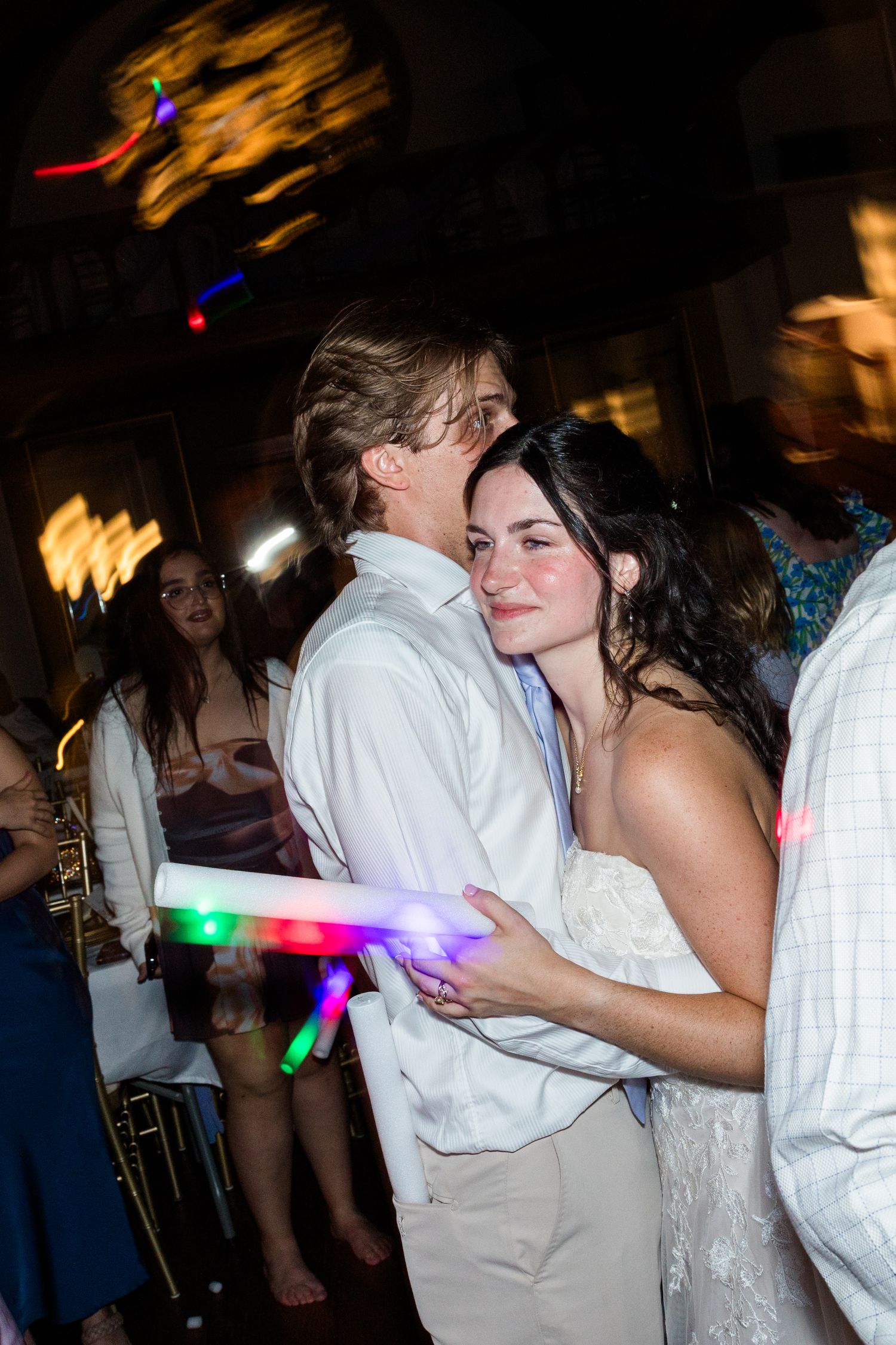 Bride and groom sharing romantic dance at wedding reception with glowing light sticks and guests.