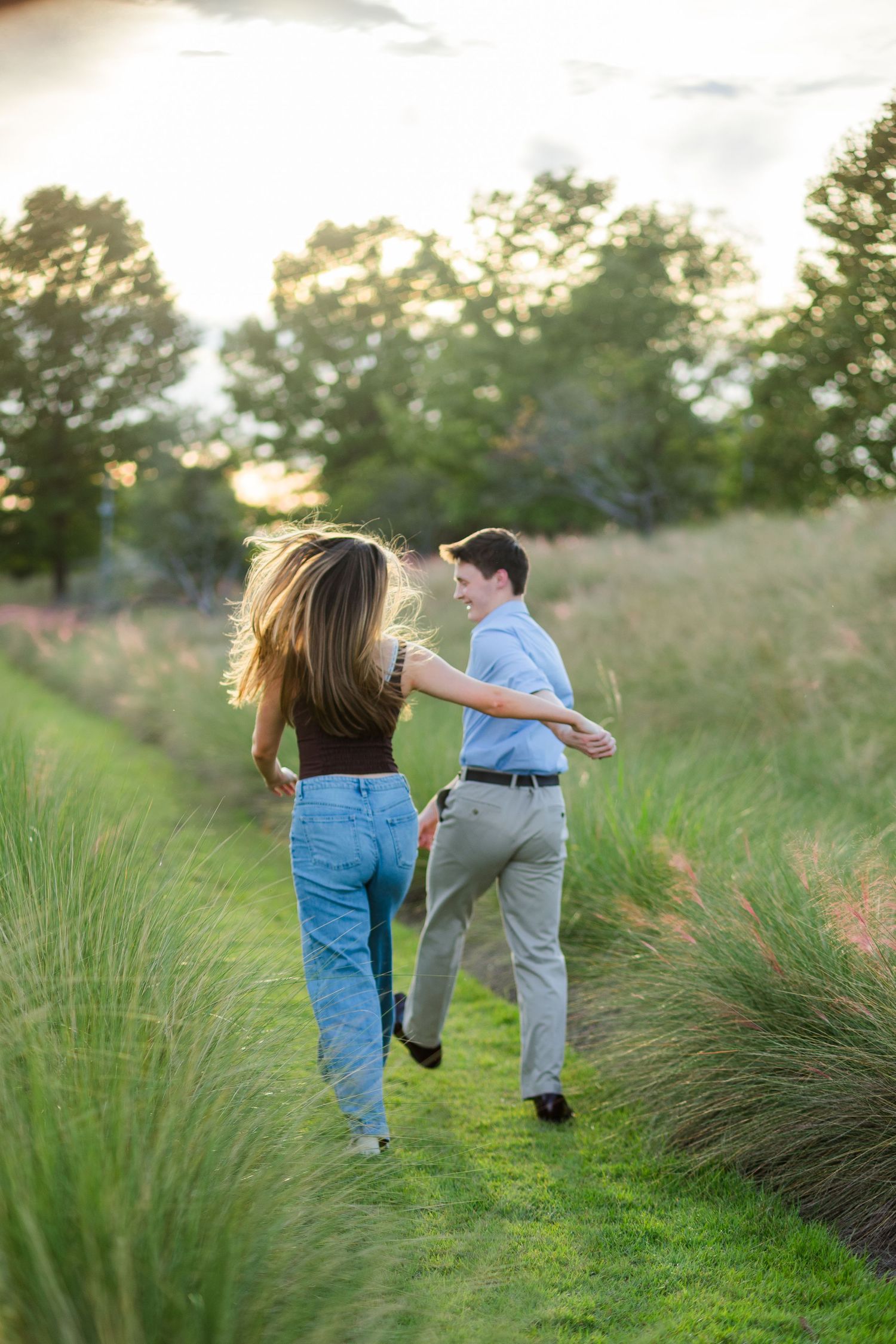 A couple walks hand-in-hand through a lush green garden path at sunset, laughing and enjoying a romantic outdoor moment.