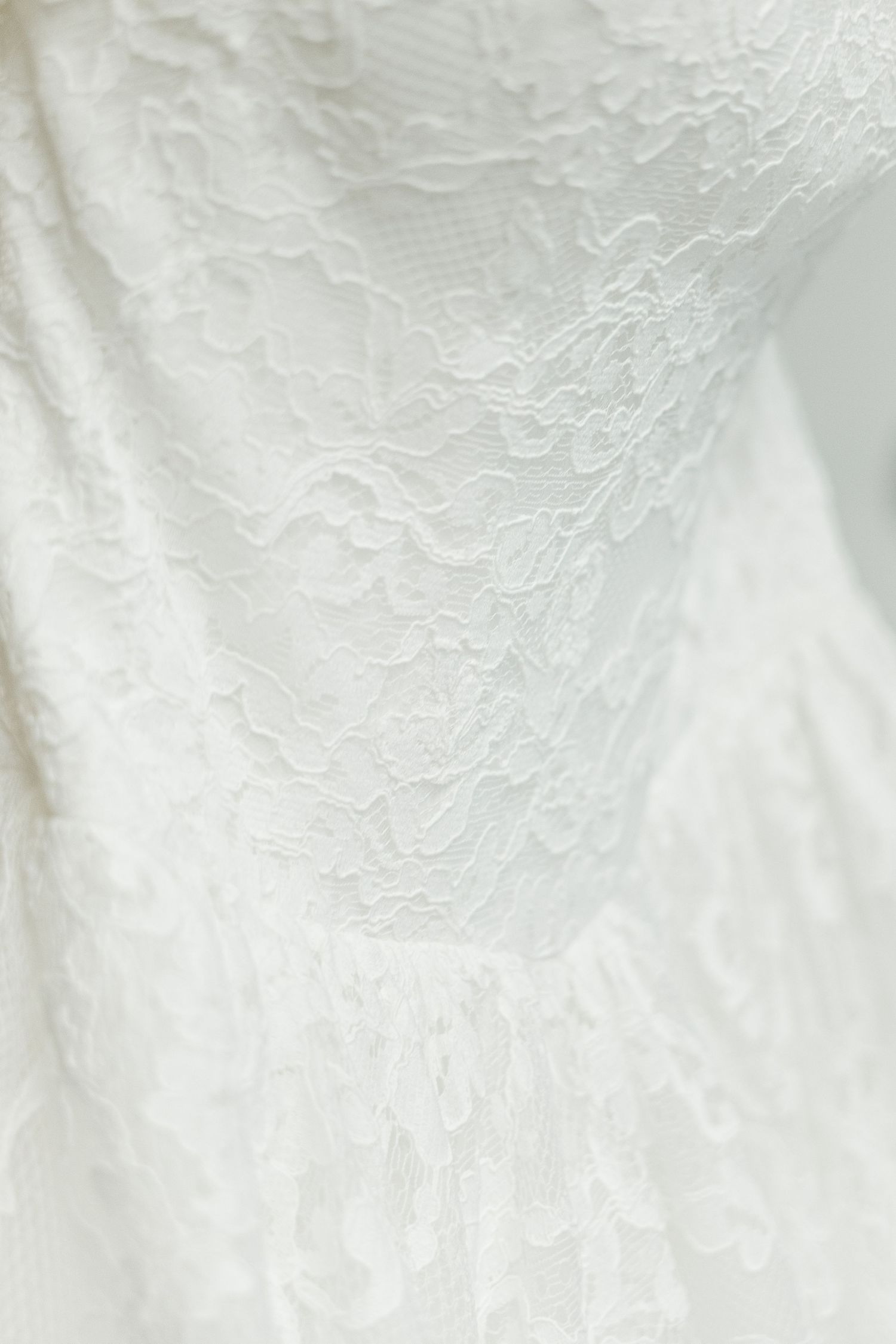 Close-up of elegant white floral lace fabric with intricate pattern details, ideal for bridal or formal wear.