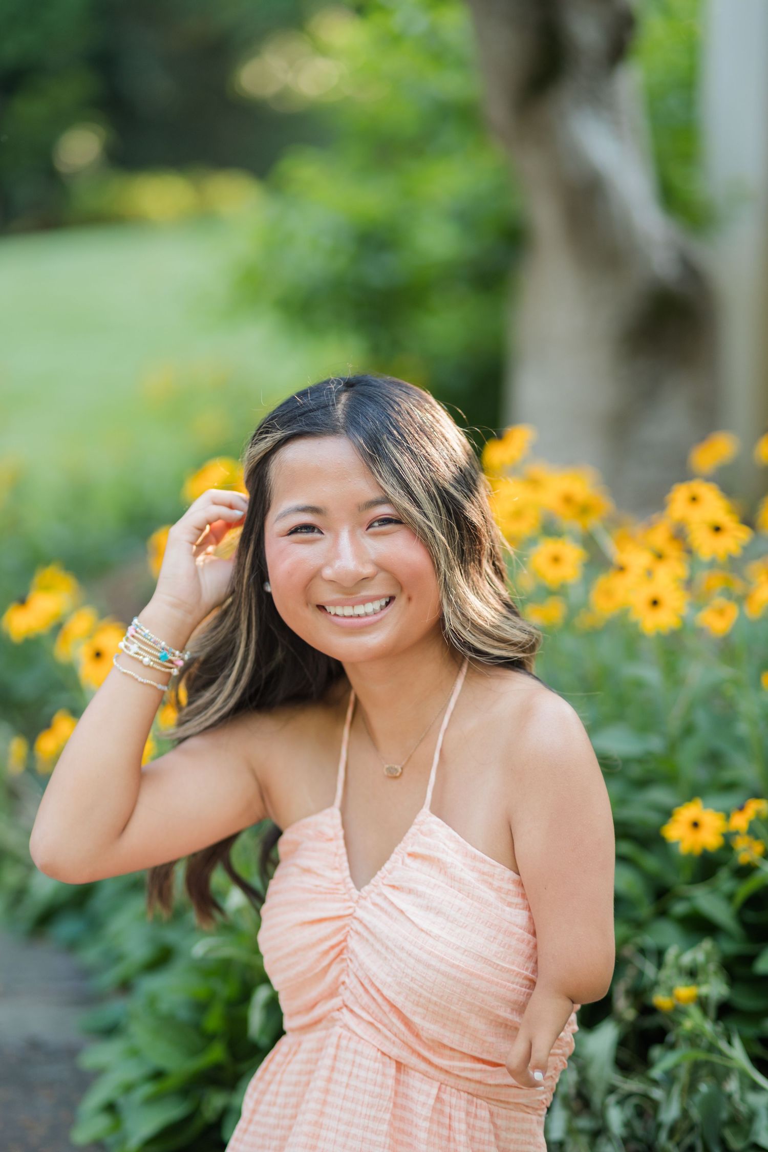 A young woman in a peach sundress laughs joyfully surrounded by yellow flowers in a garden.