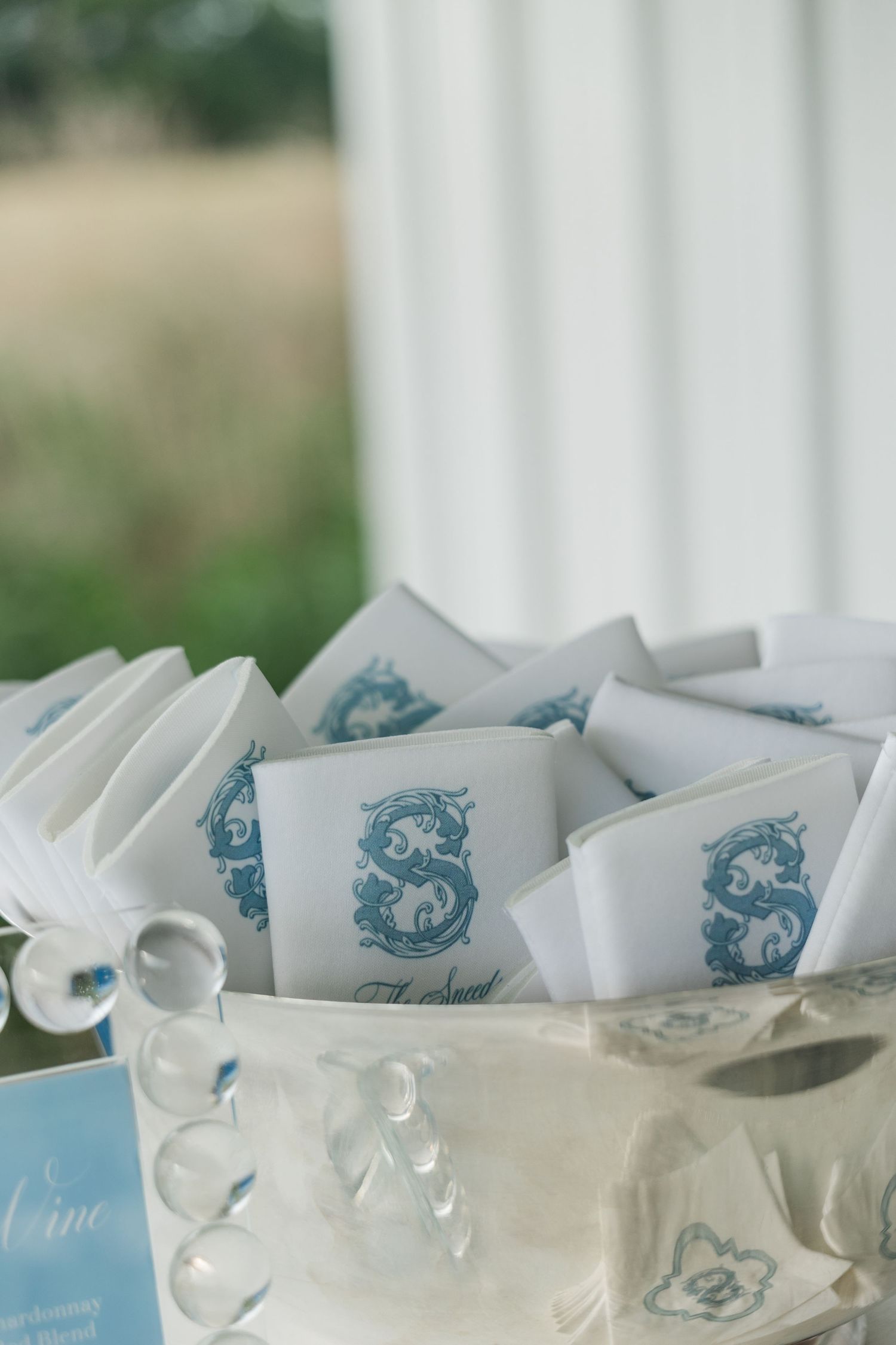White wedding programs with blue monogram S displayed in crystal bowl at ceremony entrance.