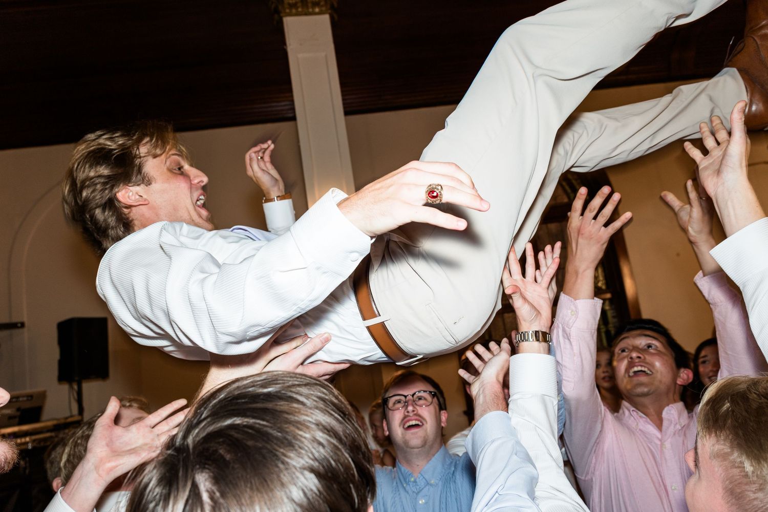 Groomsmen crowd surfing a guest during lively wedding reception celebration.