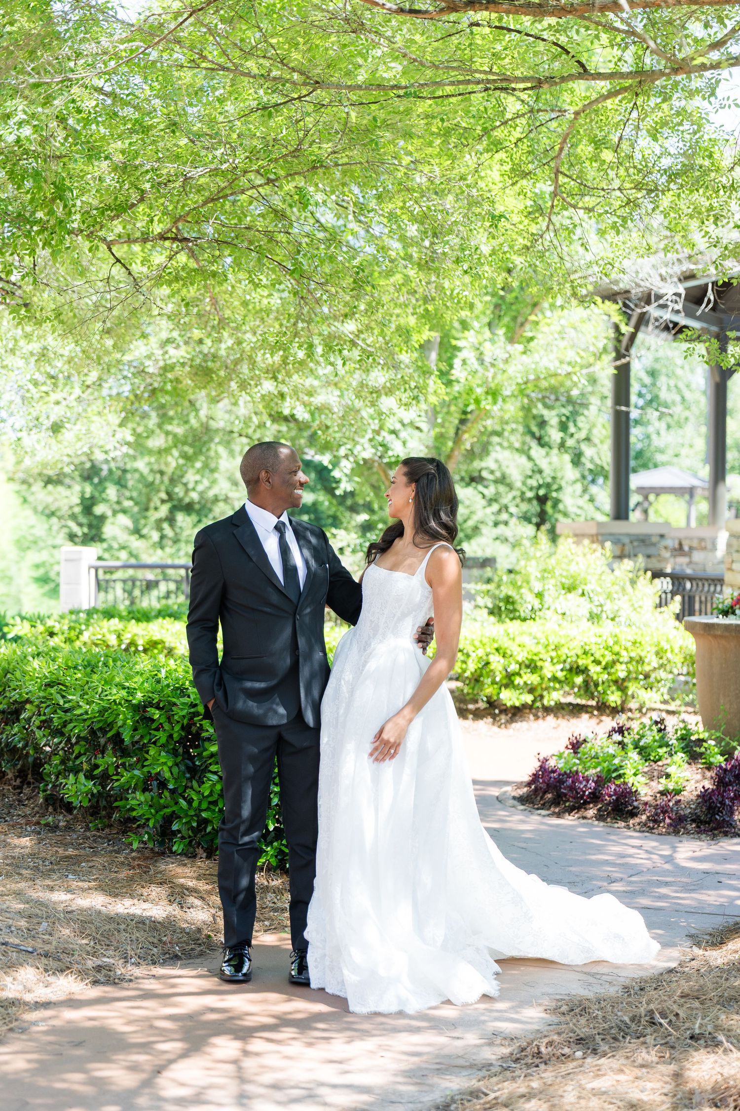 A bride and groom share a romantic moment on a garden path surrounded by lush greenery on their wedding day.