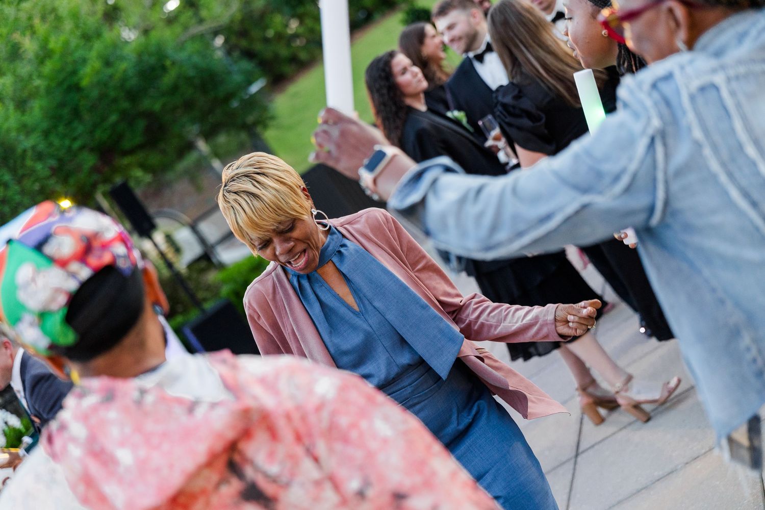 Women dancing and socializing at an outdoor event, wearing colorful attire in a garden setting.