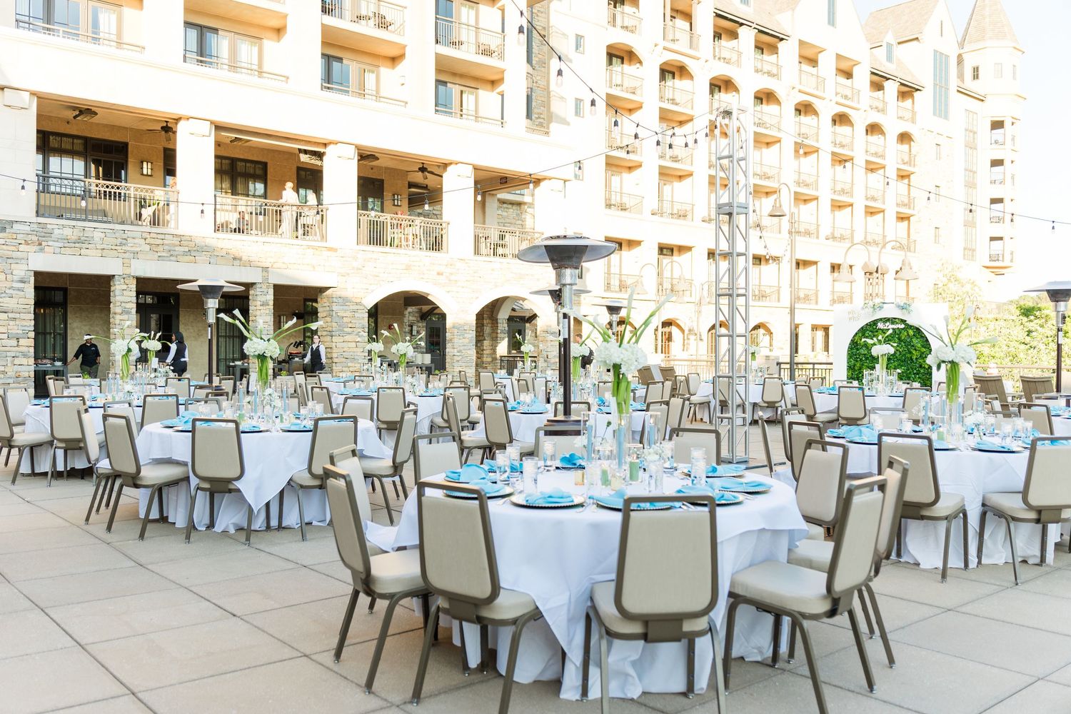Elegant outdoor wedding reception with round tables, white linens, and teal accents set on a hotel courtyard patio.