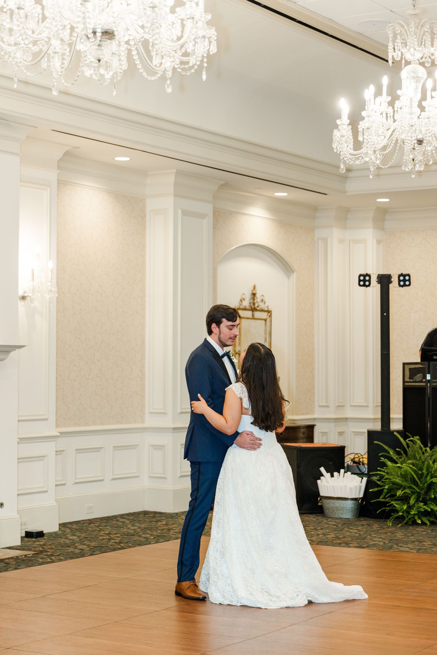 Bride and groom sharing first dance in a classic white ballroom adorned with crystal chandeliers.