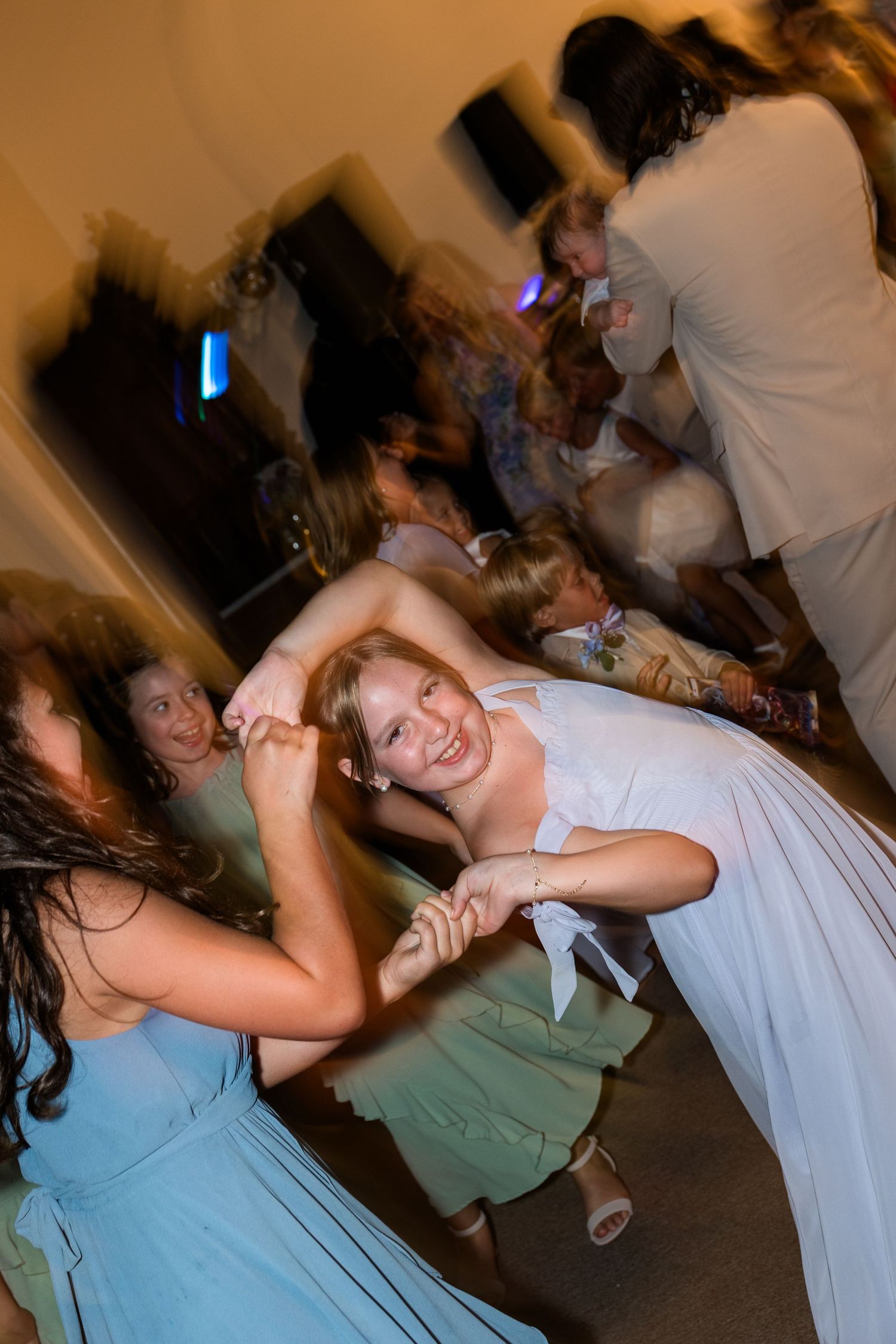 Bride in a white gown dancing and spinning joyfully with bridesmaids in blue dresses at a lively wedding reception.