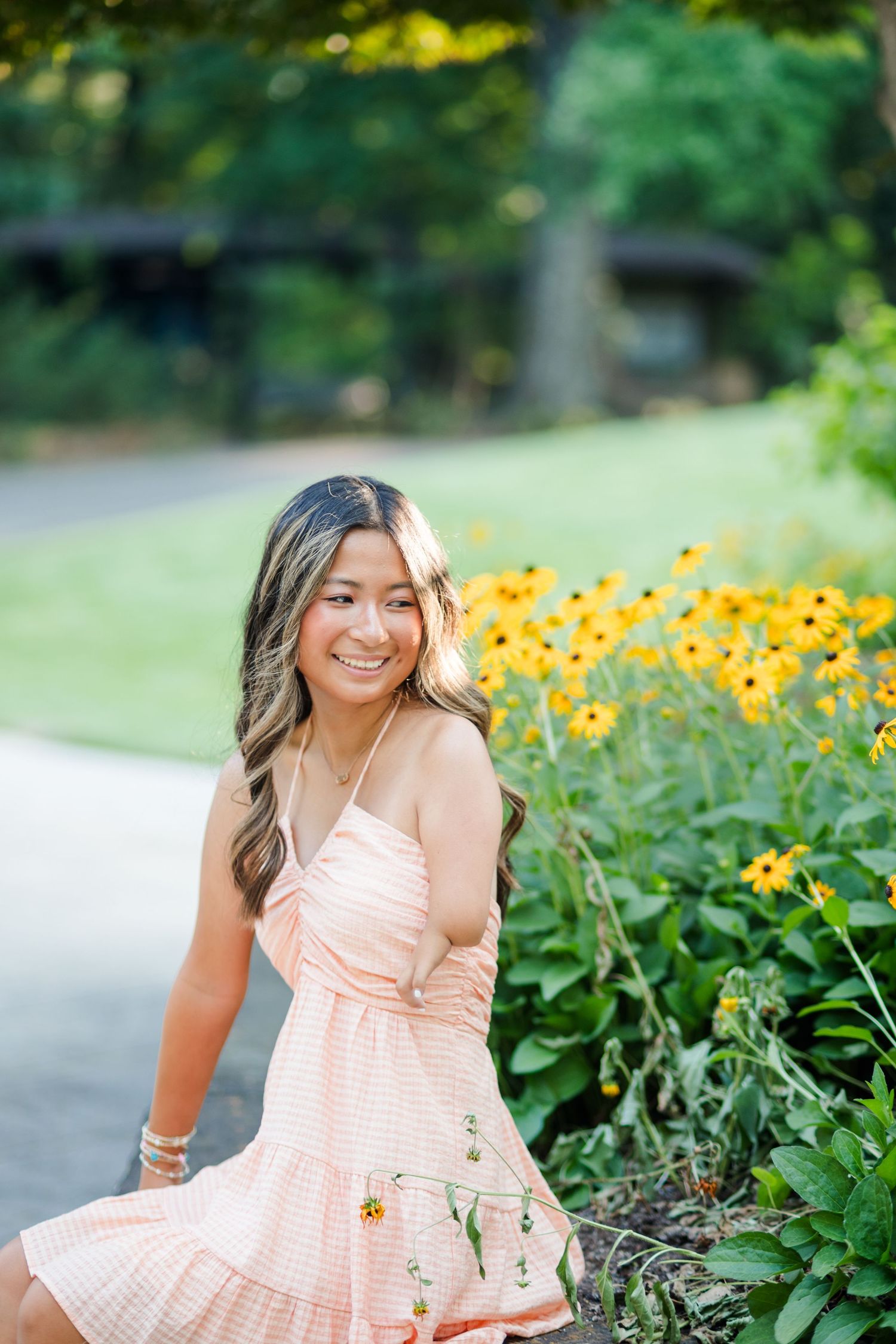 Happy young woman in pink gingham dress sitting beside black-eyed Susan flowers in park.