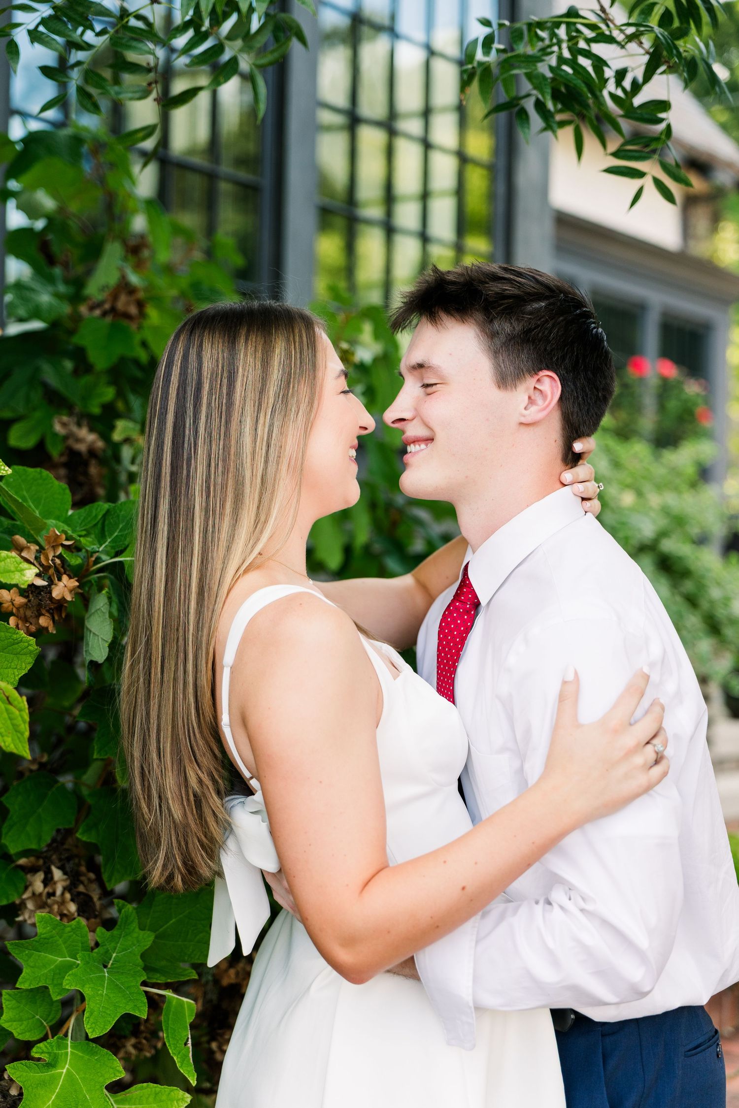 Young couple sharing a romantic moment outdoors, woman in white dress with bow, man in white shirt and red tie.