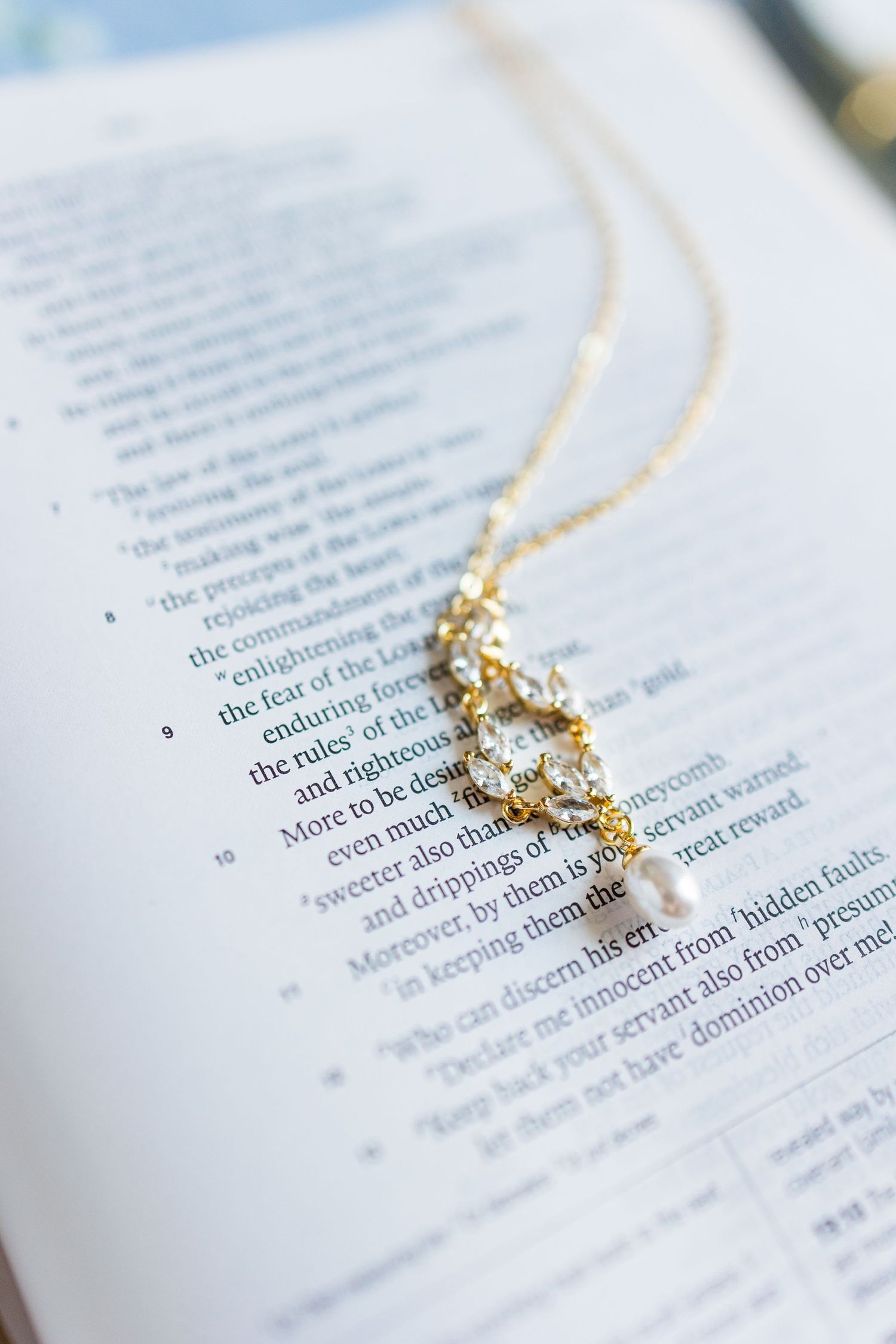 A delicate gold necklace with crystal and pearl pendant resting on an open Bible page.