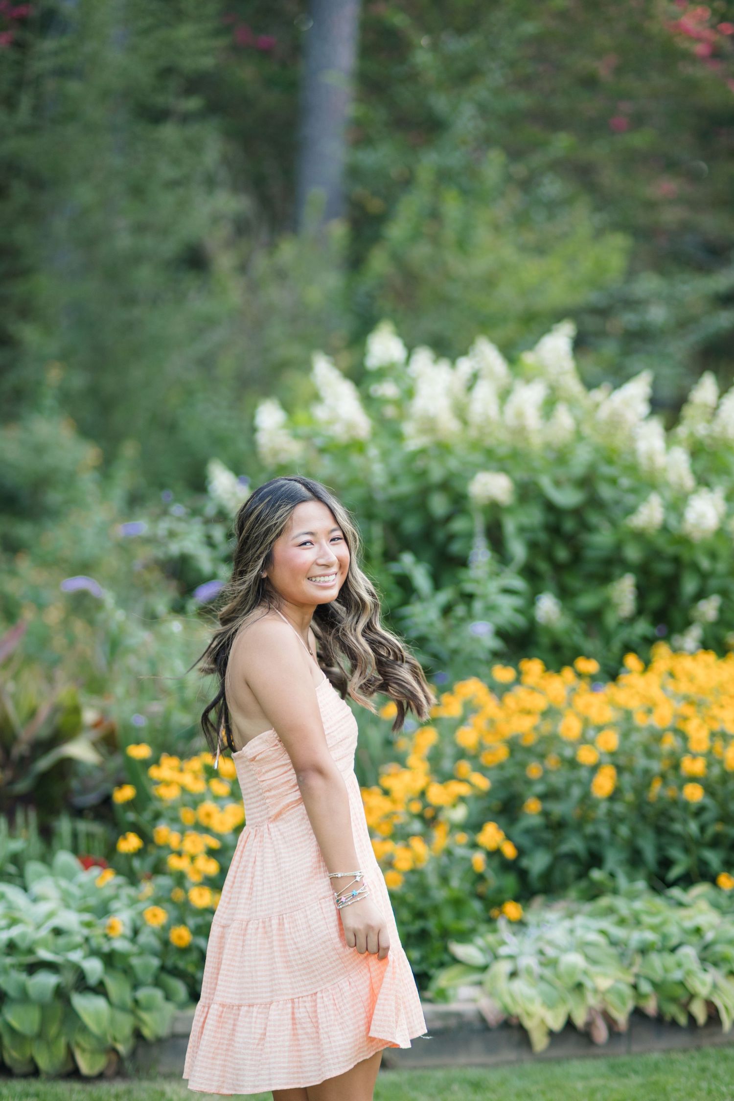 Smiling young woman in a peach dress twirling in a colorful garden with yellow flowers.