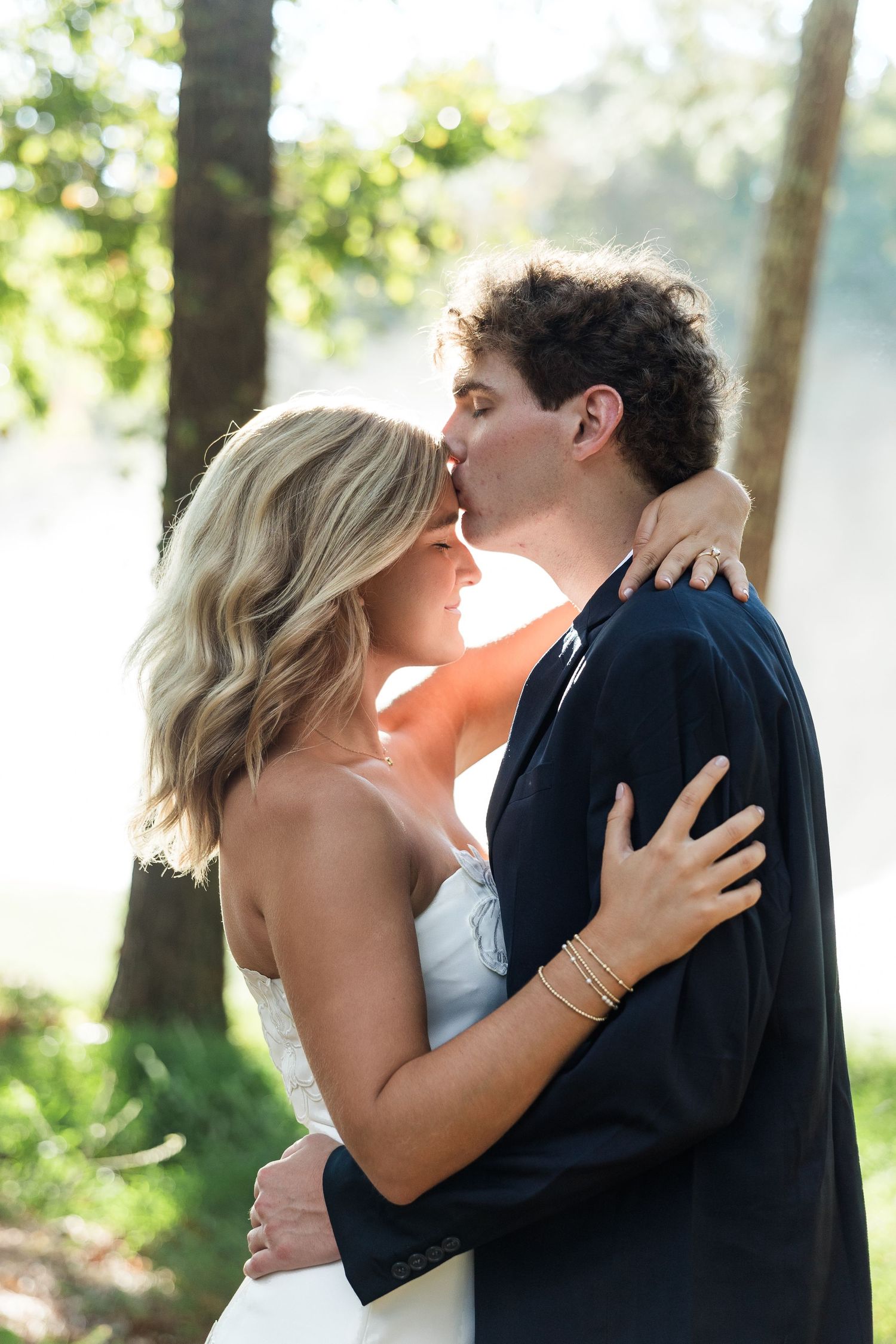 Bride and groom sharing a romantic kiss outdoors with misty bokeh background in natural light.