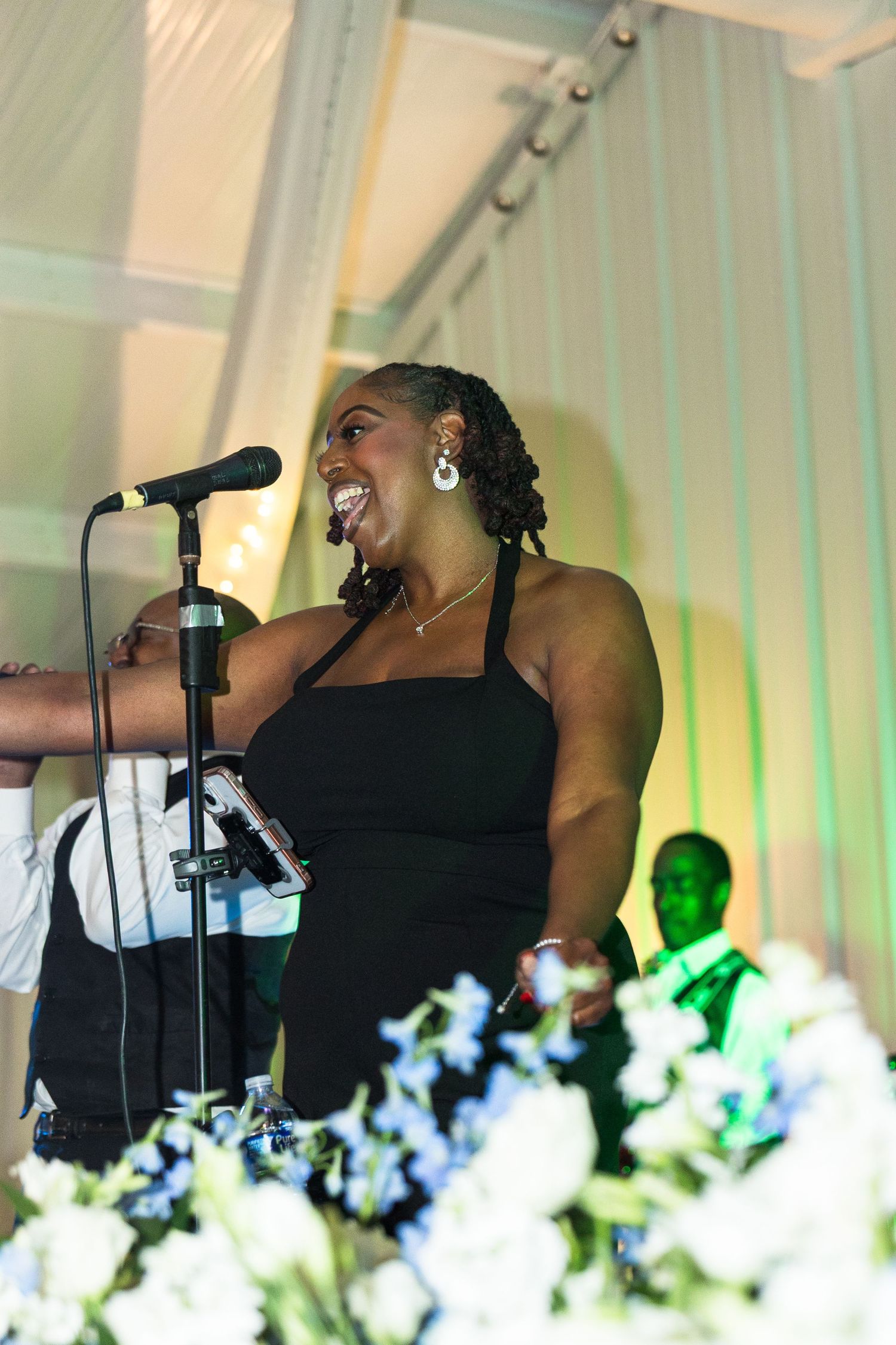 Joyful woman in black dress performing at a microphone during a wedding reception.