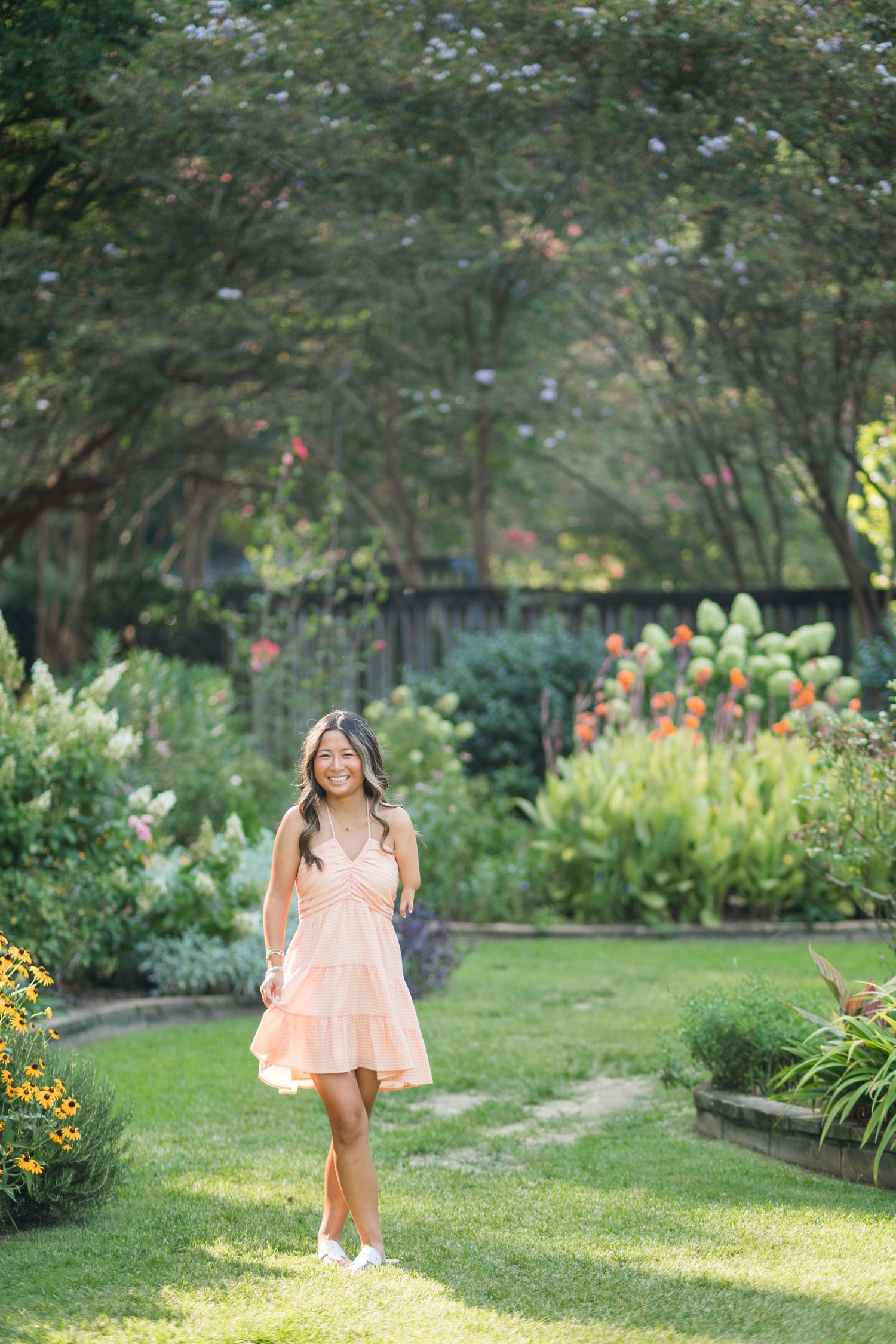 Young woman in a pink sundress walking through a lush garden with colorful flowers on a sunny day.