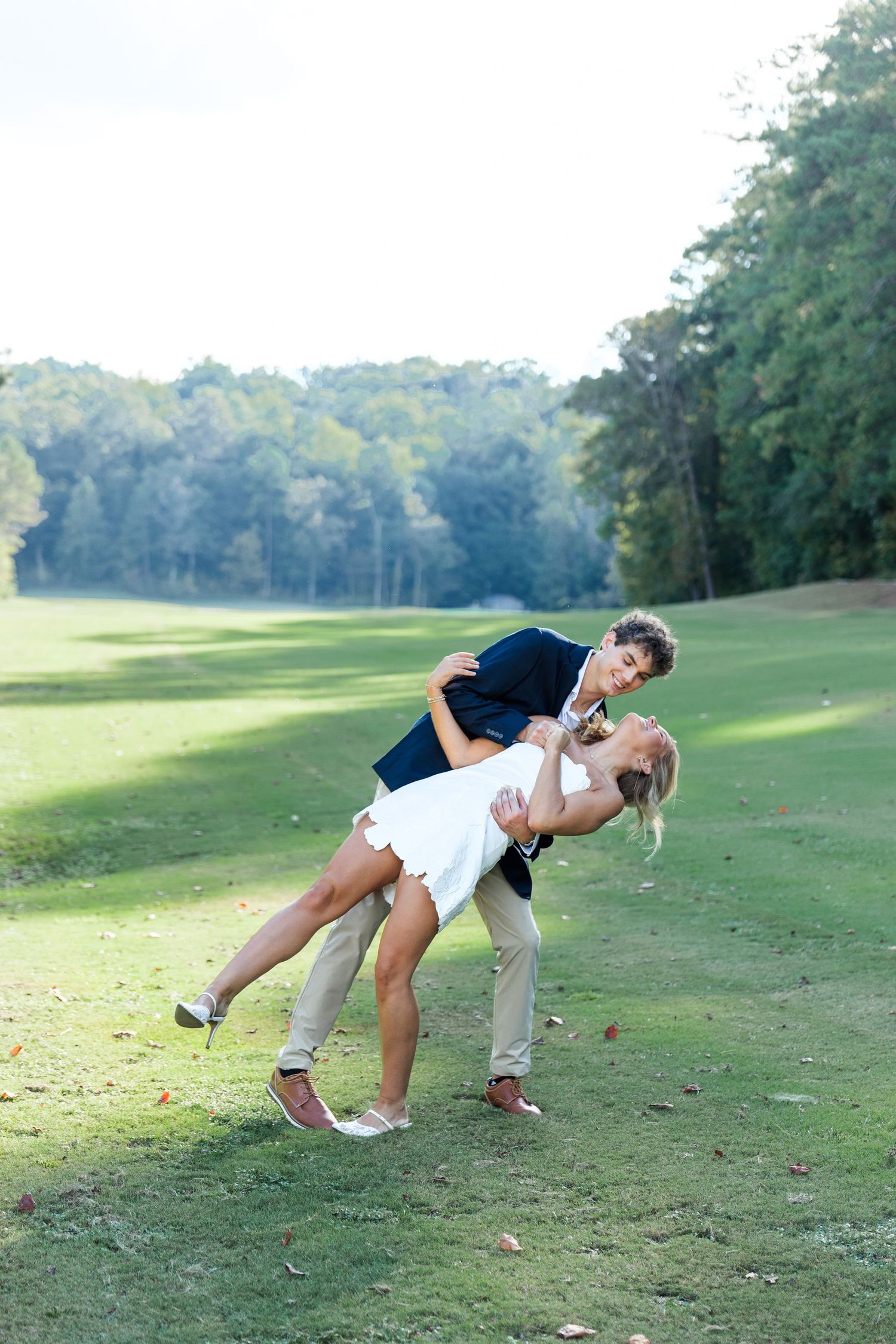 Bride and groom share a romantic dip pose on a lush green golf course surrounded by trees.