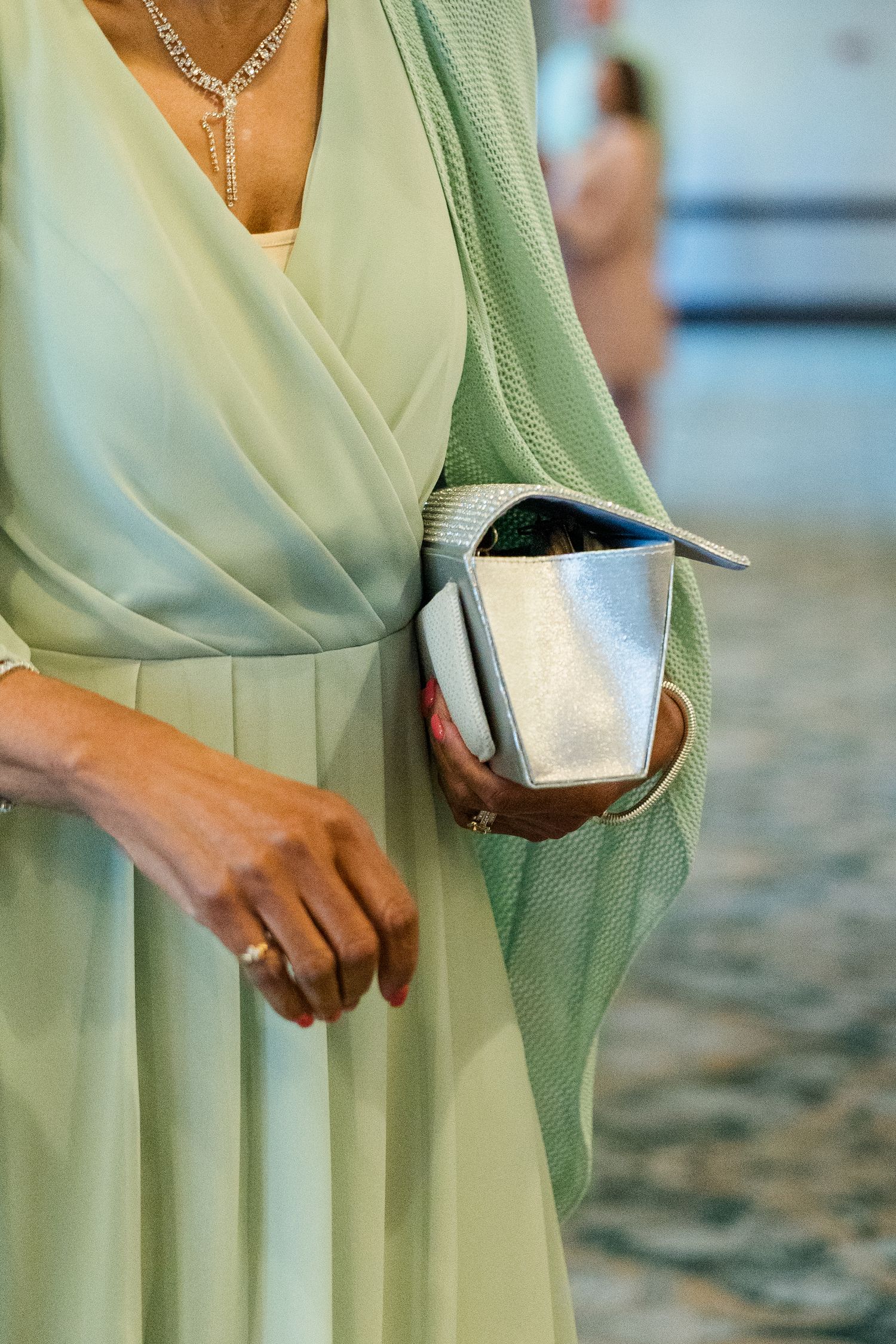 Woman in mint green dress holding silver clutch purse at formal event.