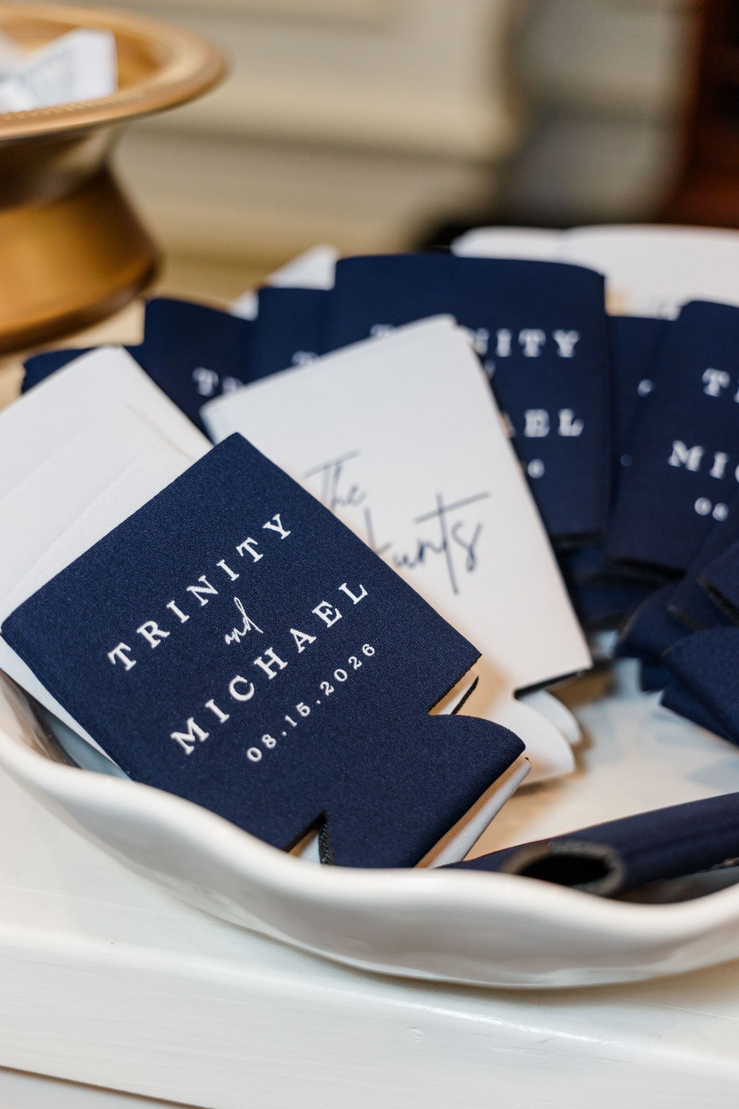 Navy blue custom wedding koozies reading Trinity and Michael 08.15.2026 displayed in a white bowl.