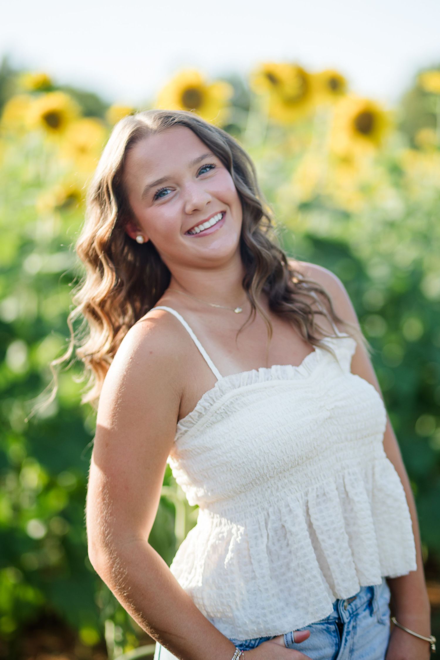 Smiling young woman in white crop top posing in sunflower field on a sunny day.