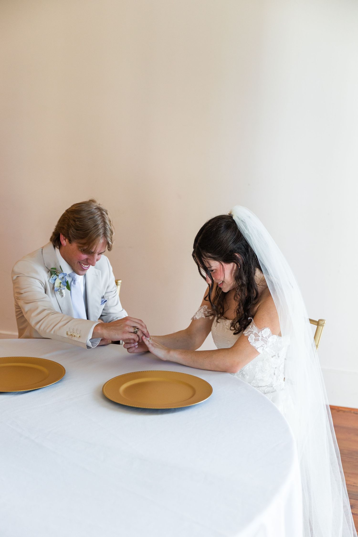 Bride and groom hold hands at wedding reception table with gold charger plates in elegant venue.