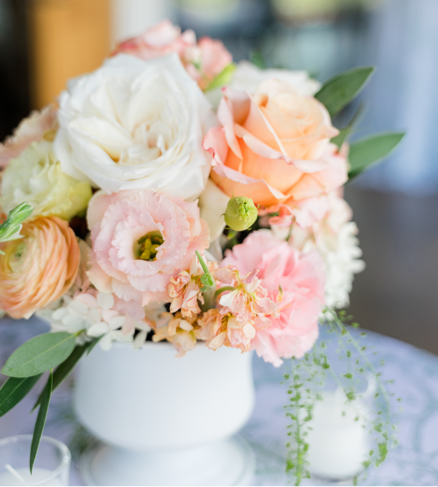 Elegant floral arrangement with peach roses, pink ranunculus, and white blooms in a white vase centerpiece.