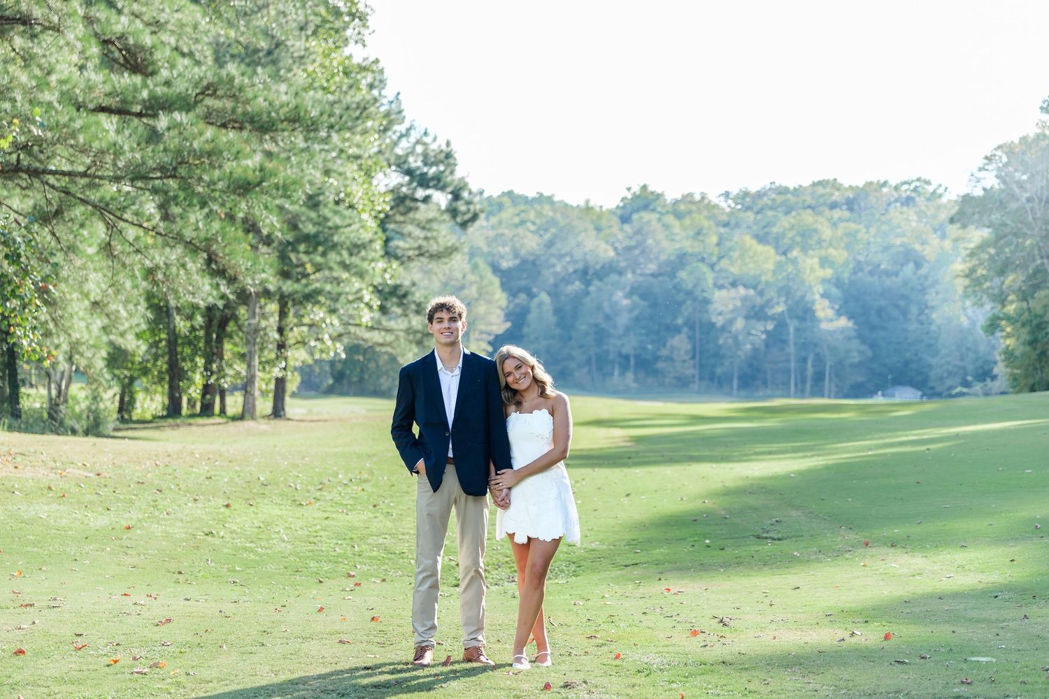 Couple posing together on a sunny golf course surrounded by lush green trees and grass.