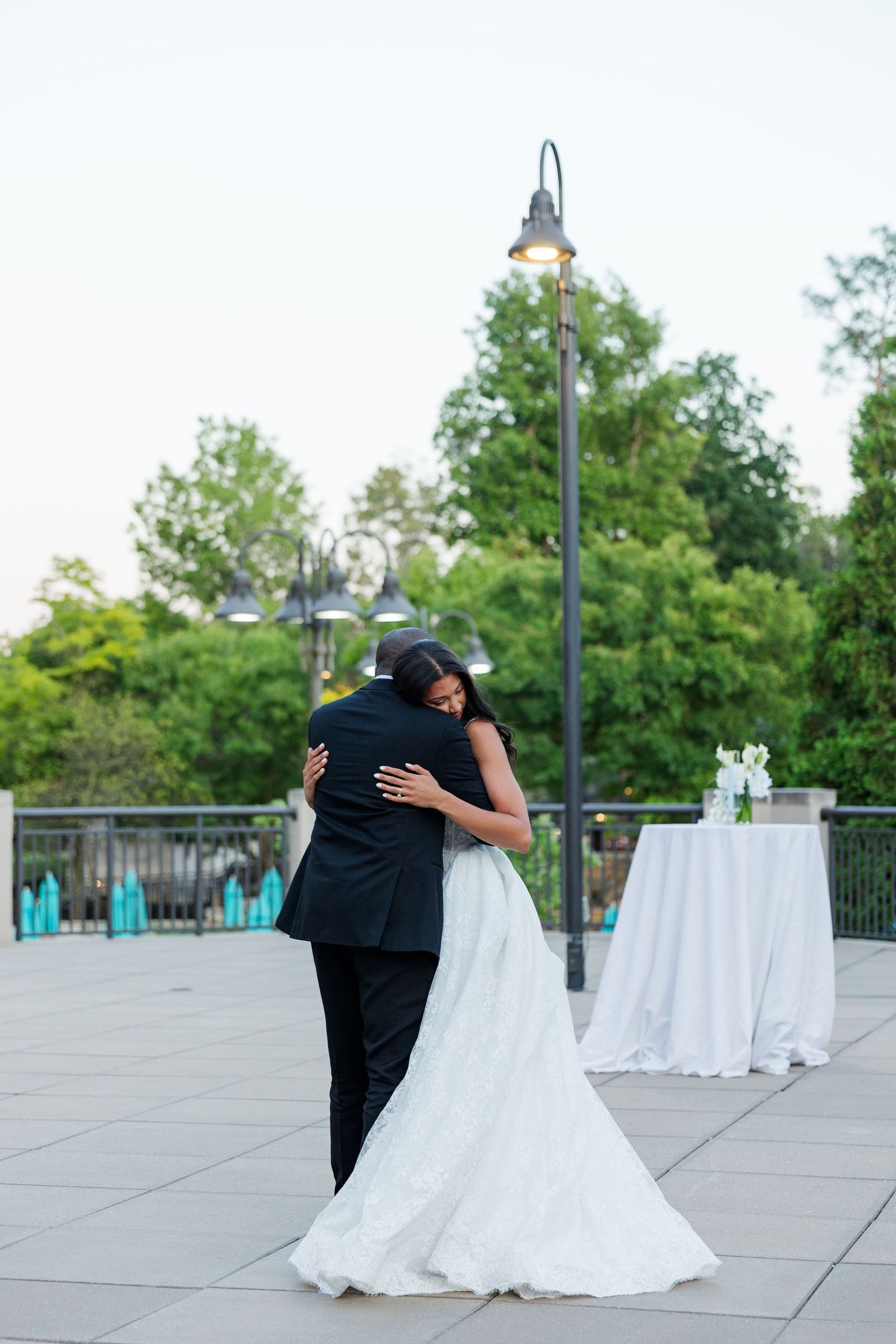A bride and groom share their first dance outdoors on a patio at dusk, embracing tenderly in wedding attire.