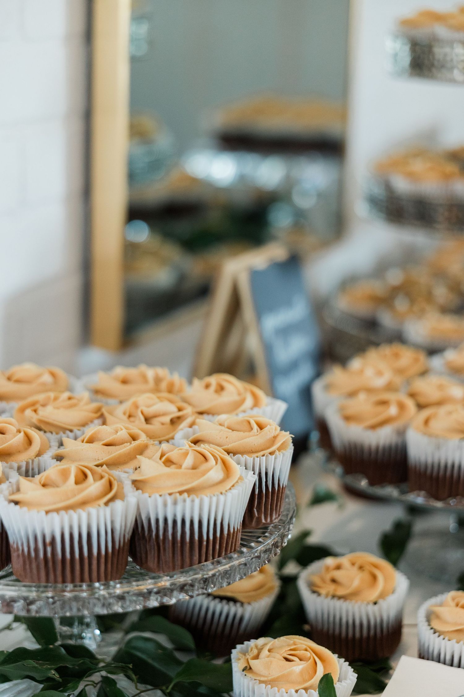 Elegant wedding dessert table featuring cupcakes with swirled caramel frosting displayed on crystal cake stands.