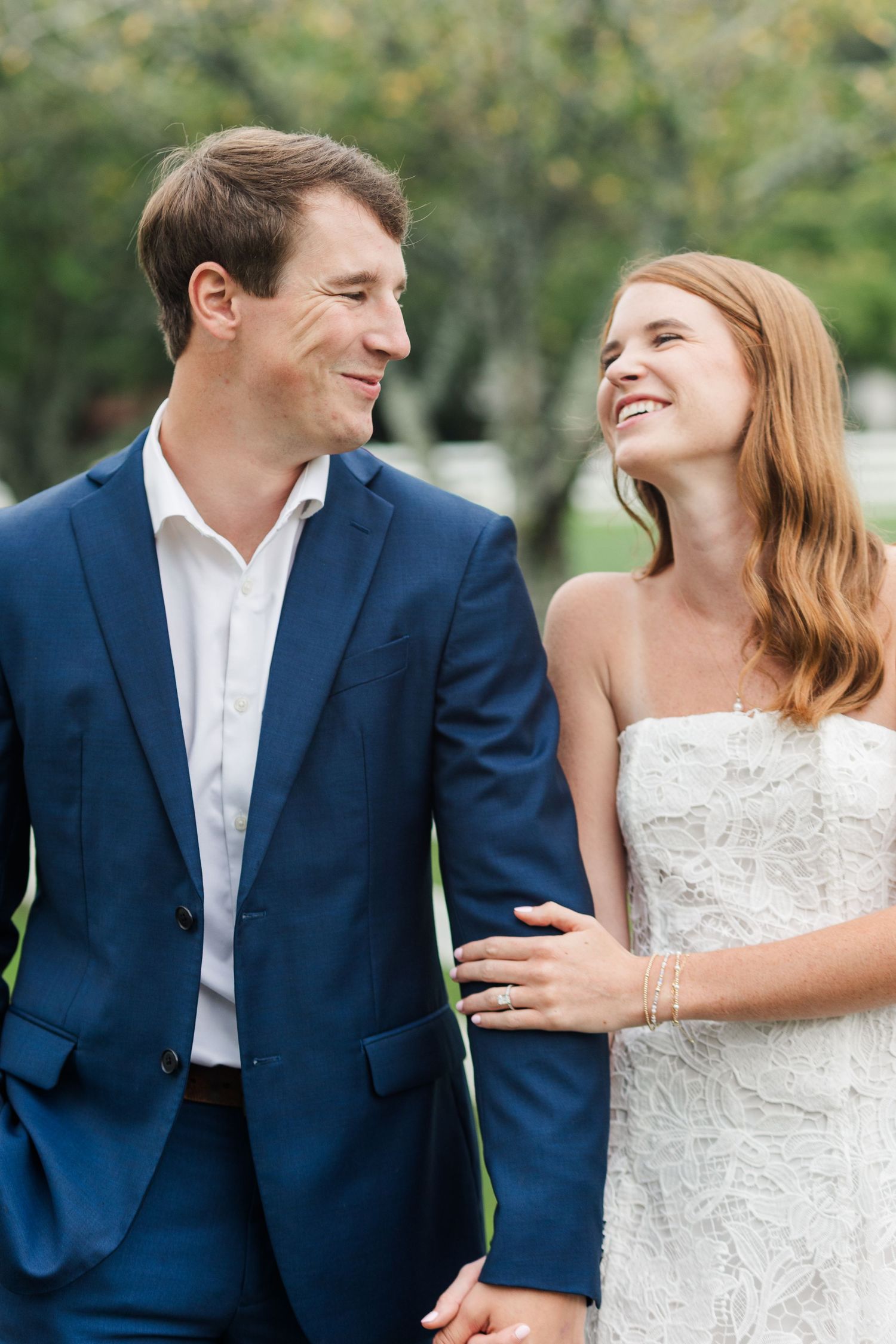Smiling bride and groom in navy suit walking together outdoors on their wedding day.